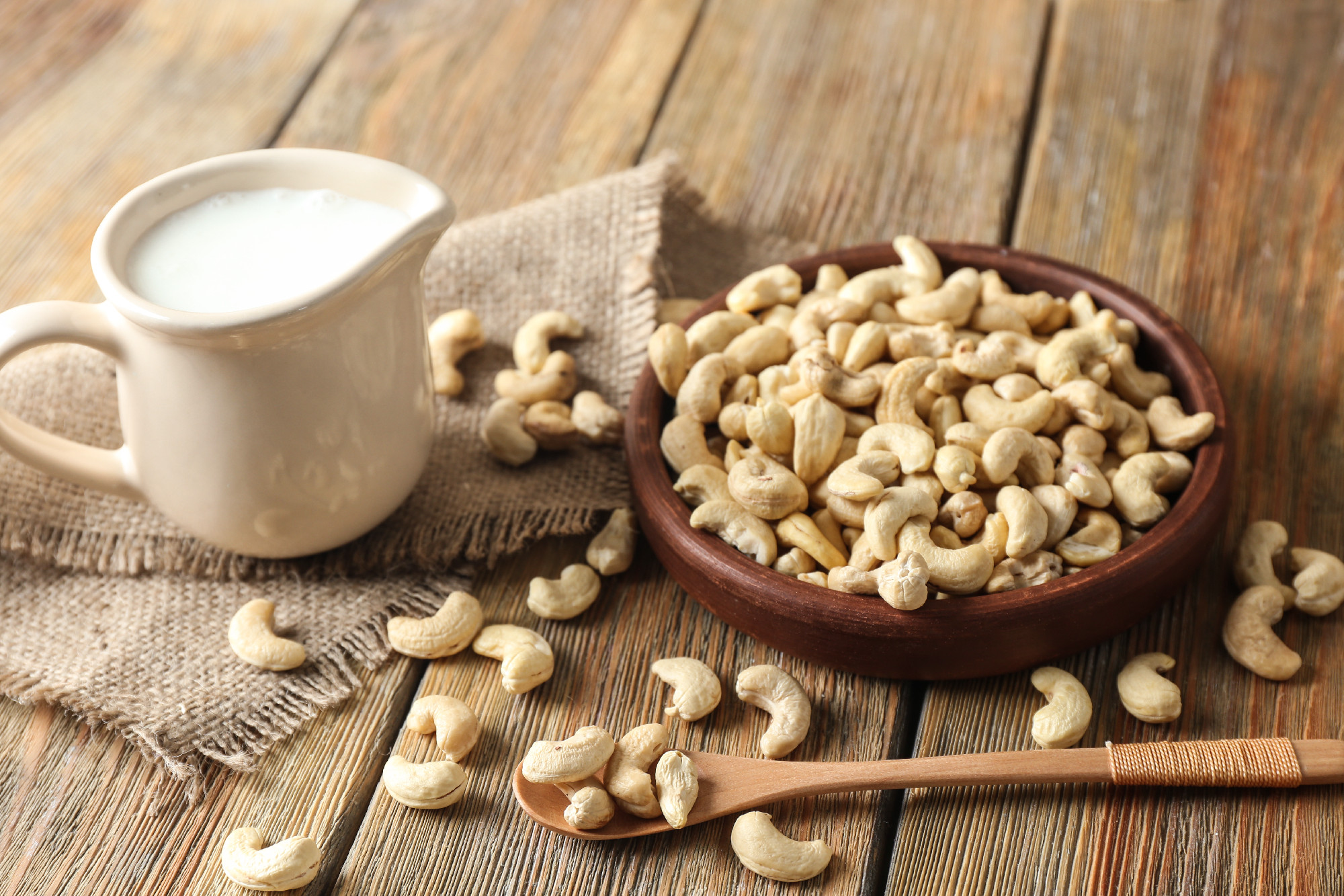 Plate with tasty cashew nuts and jug of milk on wooden table�