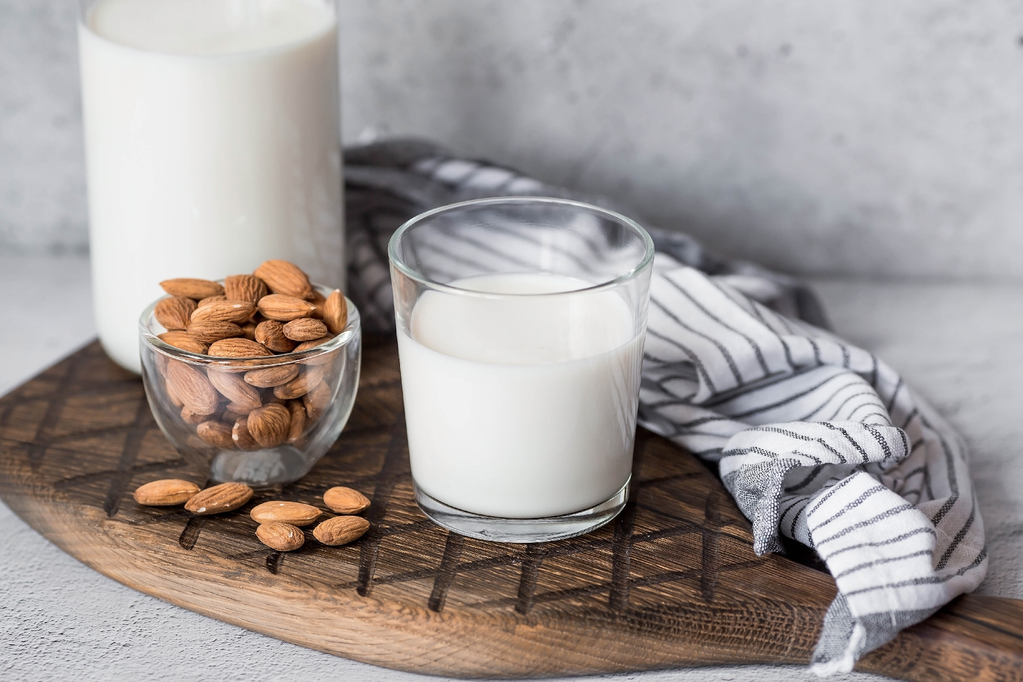 Organic almond milk in a glass bottle next to an almond on a stylish wooden board on a stone table. Natural eco-friendly products.