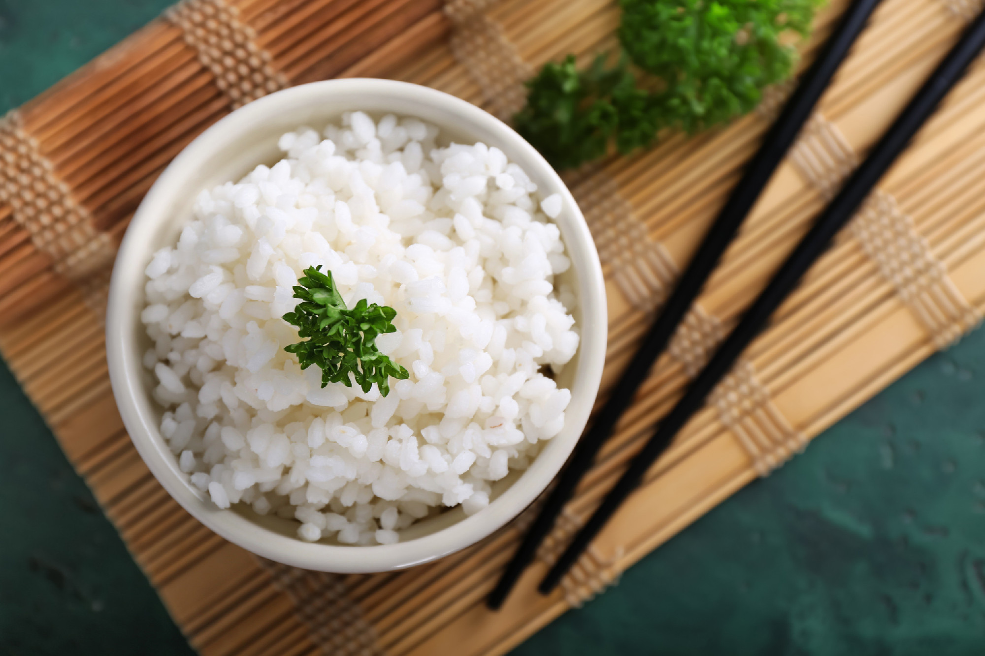 Bowl with boiled white rice and chopsticks on bamboo mat�