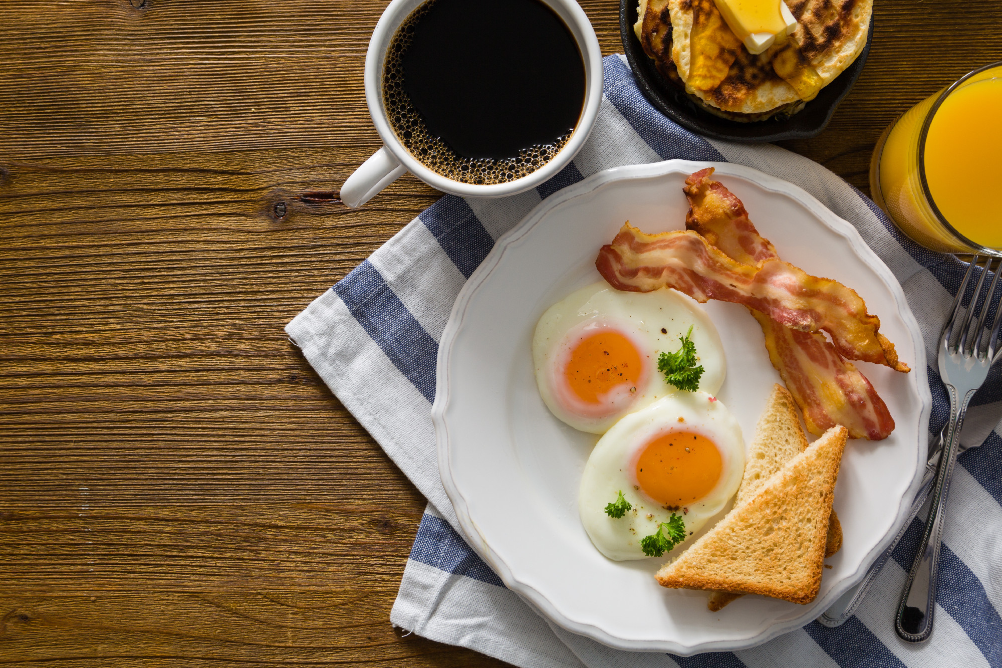 American breakfast with sunny side up eggs, bacon, toast, pancakes, coffee and juice