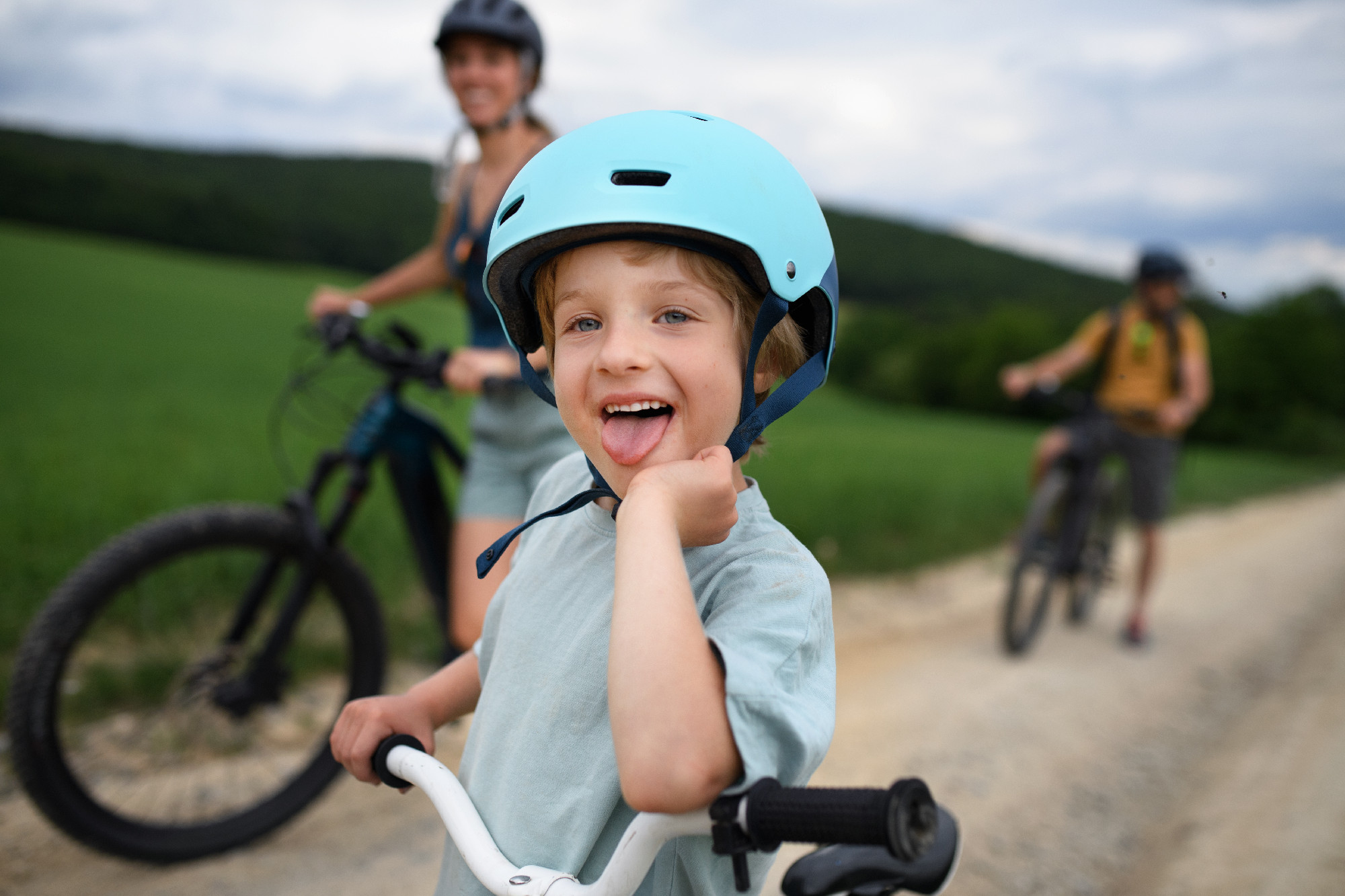 Portrait of excited little boy with his family at backround riding bike on path in park in summer