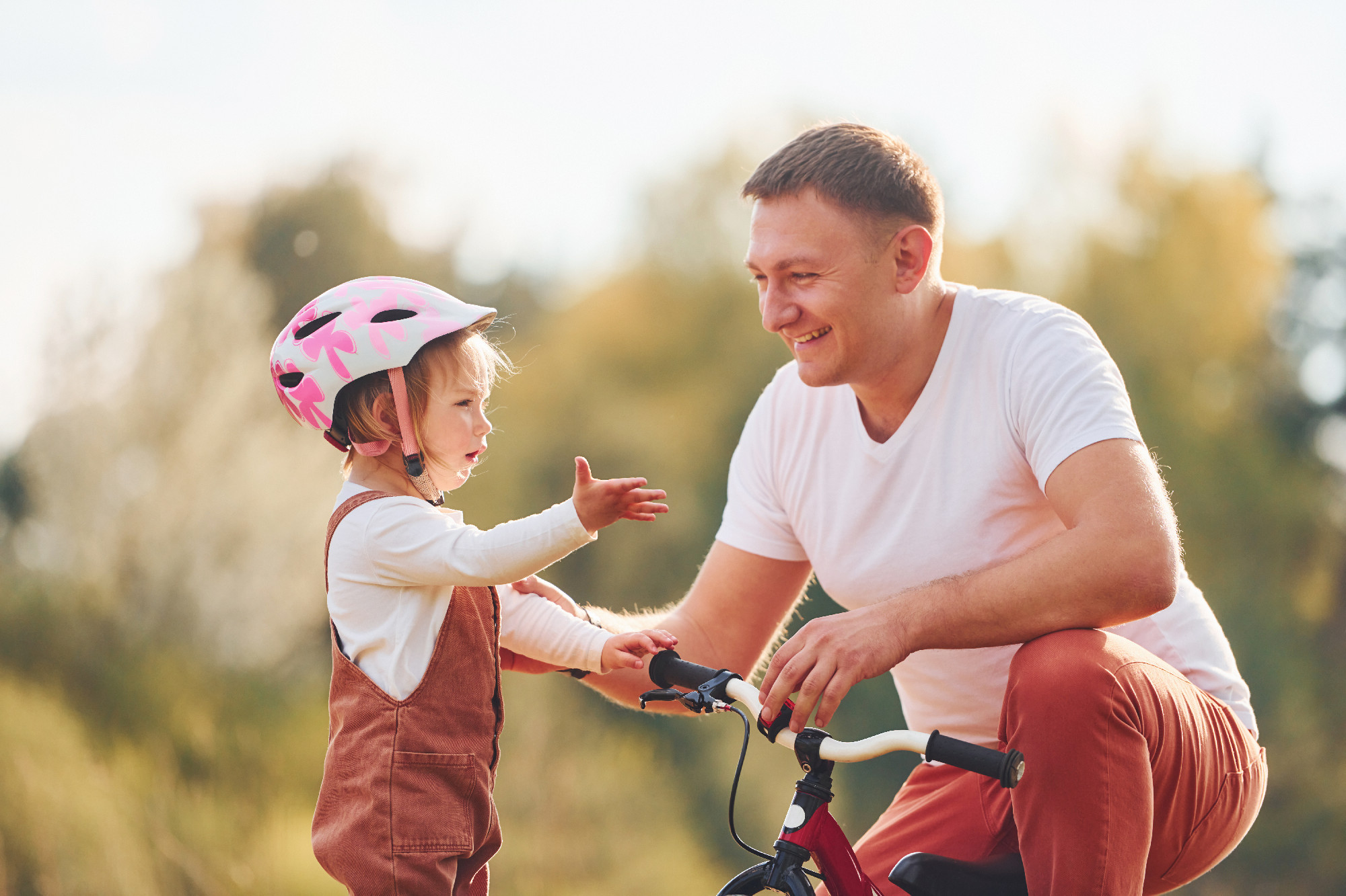 Beautiful sunlight. Father in white shirt teaching daughter how to ride bicycle outdoors