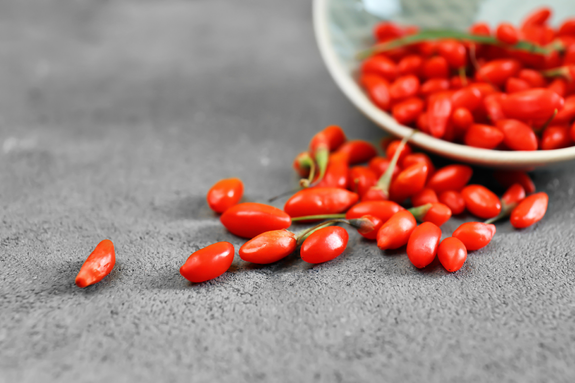 Fresh goji berries scattered from bowl on table�