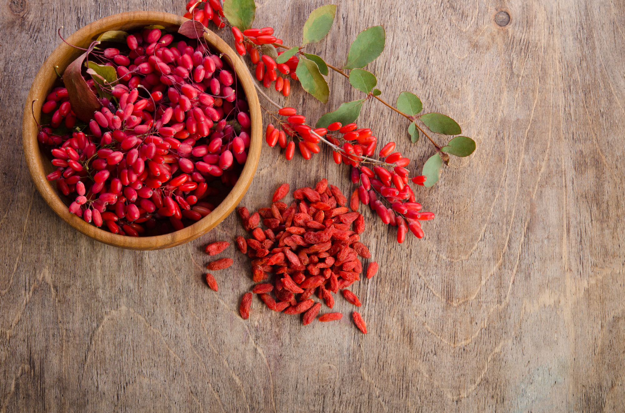 Barberry with leaves and dry goji berries on wooden background
