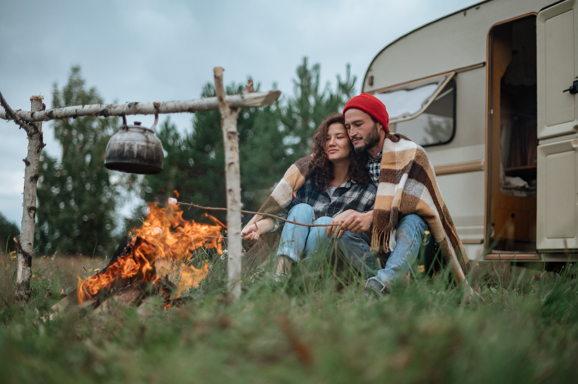 Couple in a checkered plaid roasting marshmallows on fire near the trailer home.