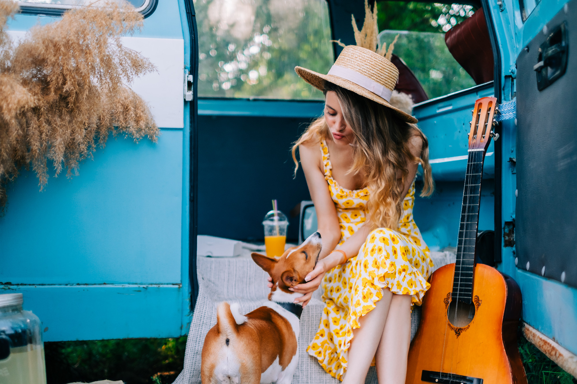 Portrait of cheerful young woman with her dog outdoors near van, simmer traveling concept.