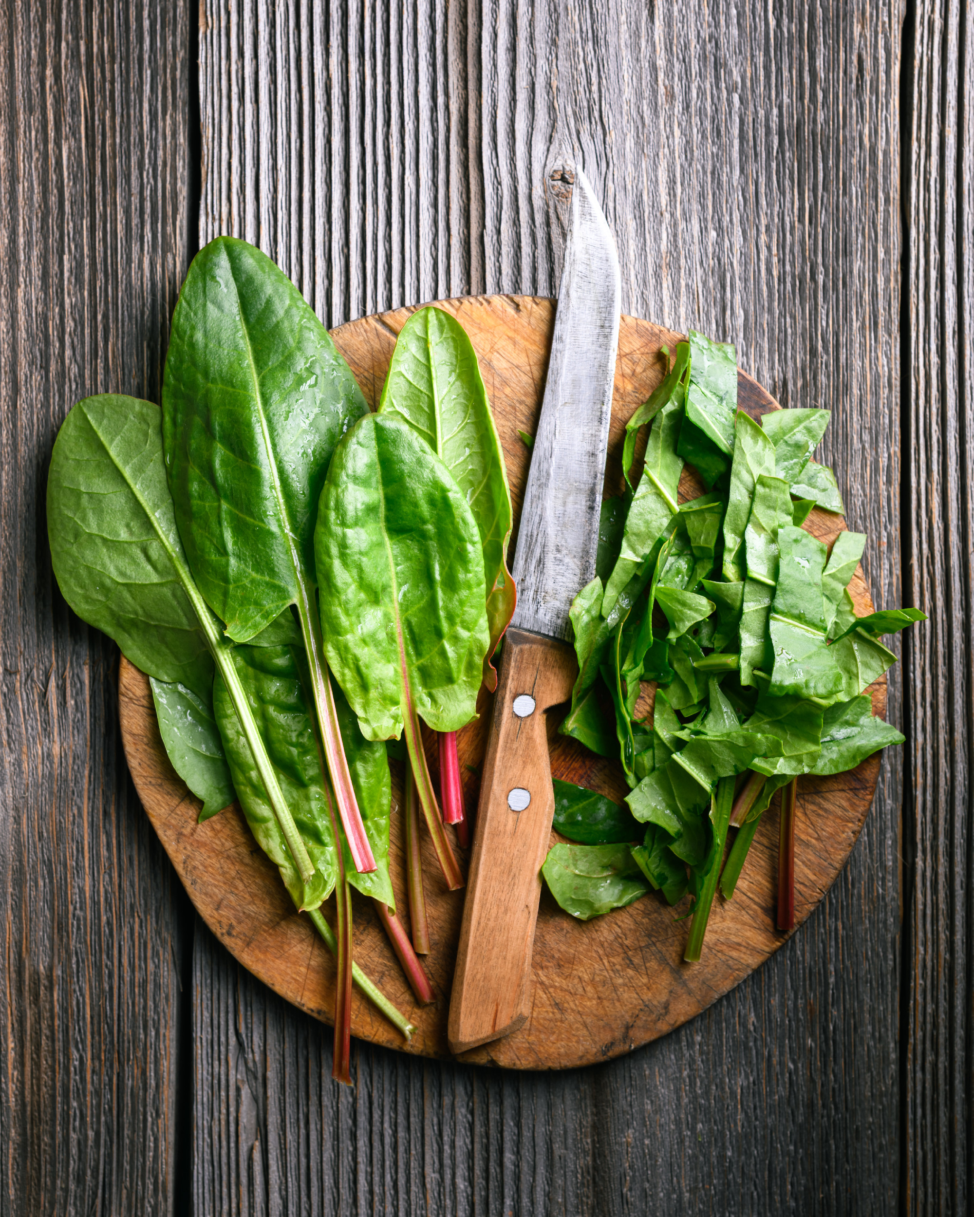 Slicing green sorrel leaves on a rustic wooden cutting board