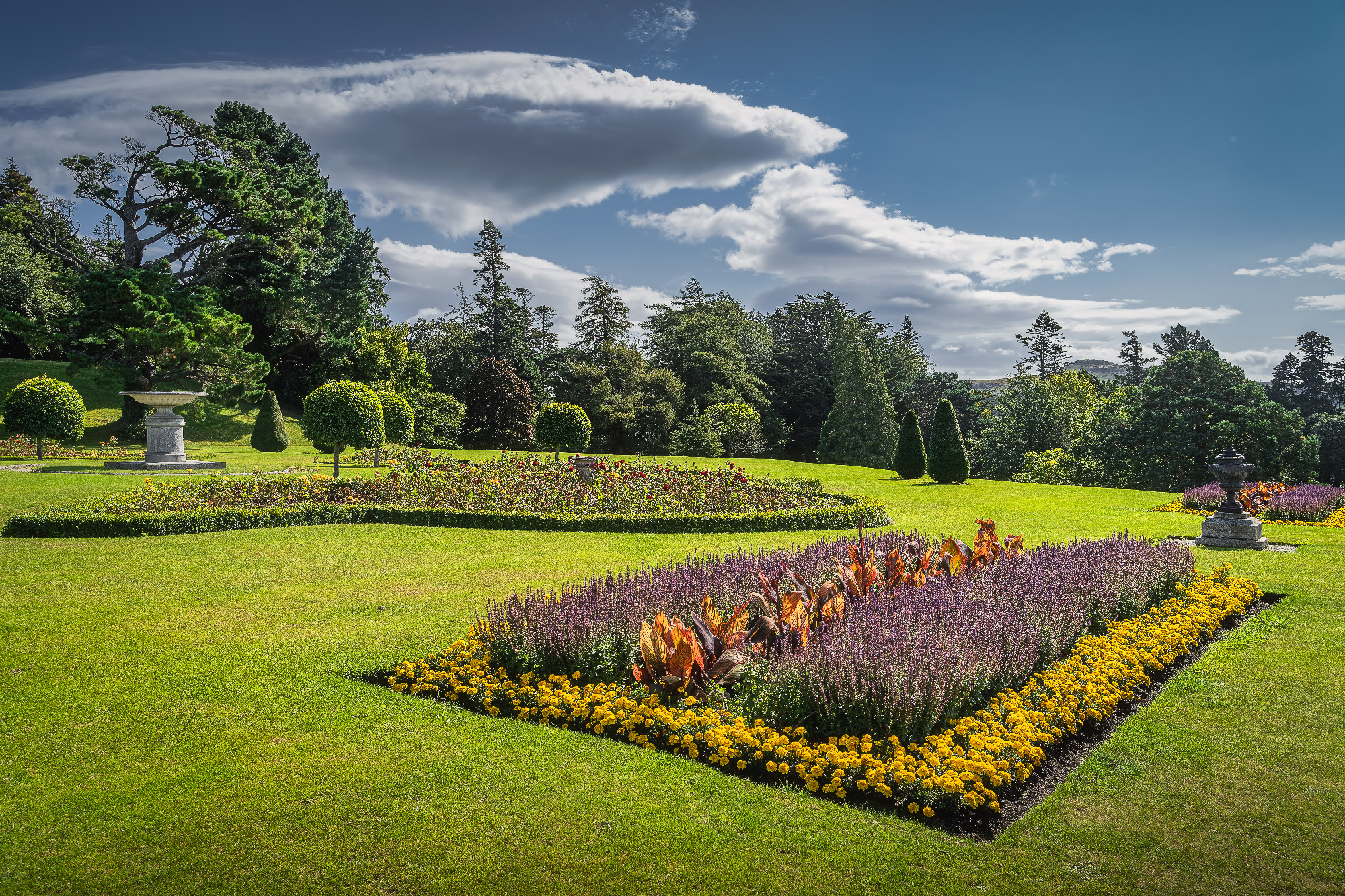 Powerscourt garden with flowerbeds, hedges, decorative trees, fountains and forest in the background, Ireland