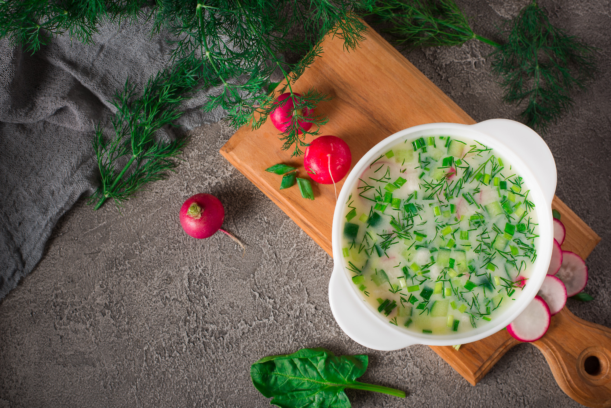Summer yoghurt cold soup with radish, cucumber, and dill on wooden table. Okroshka