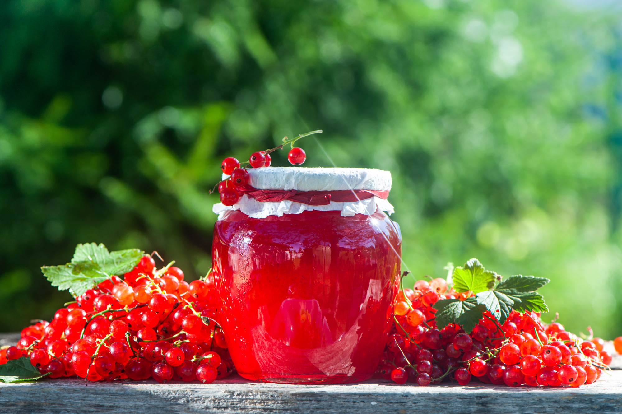 Red, juicy berries of red currants and jars of berry jam on a wo
