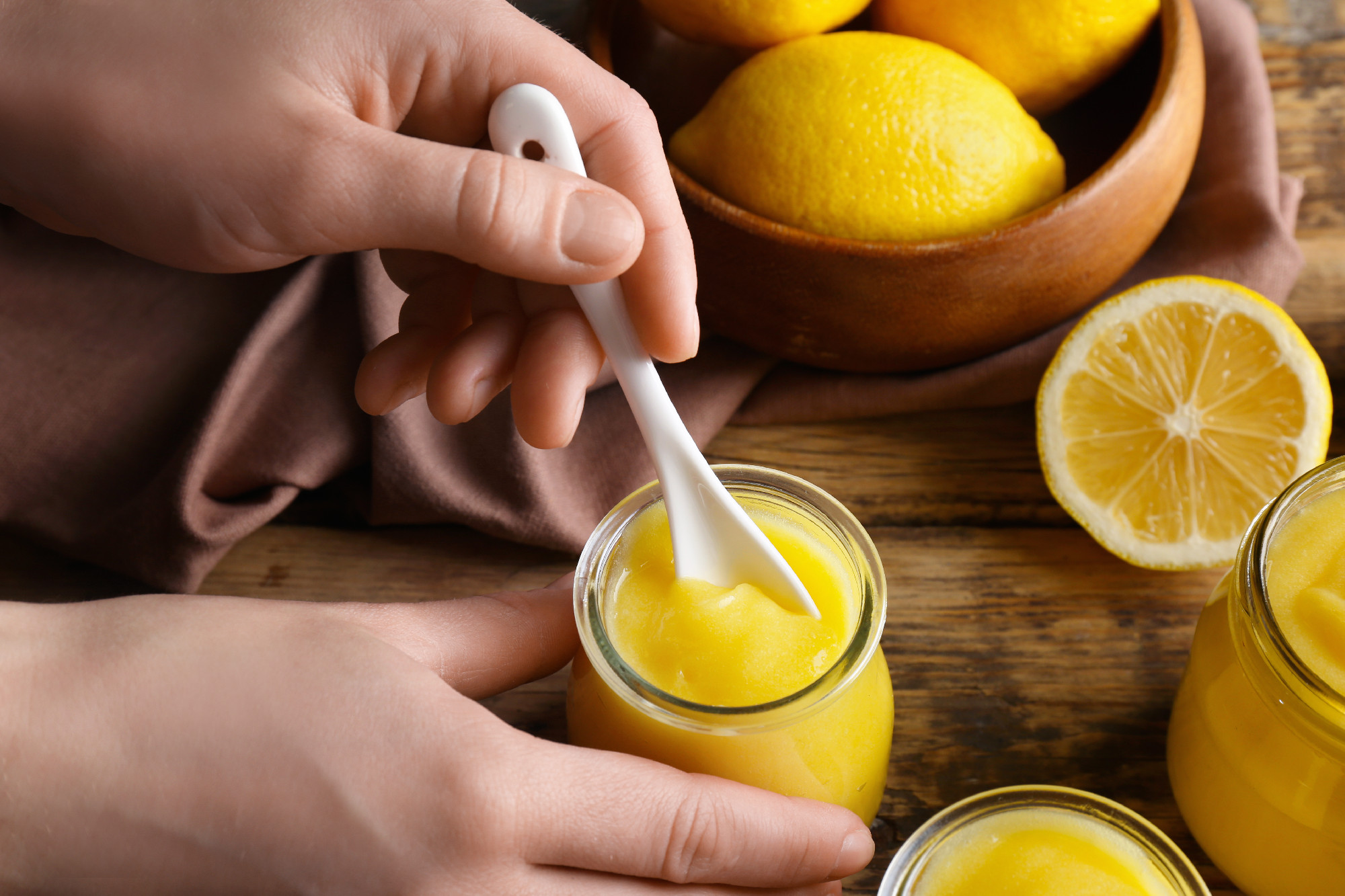 Woman taking lemon curd from glass jar on wooden background�