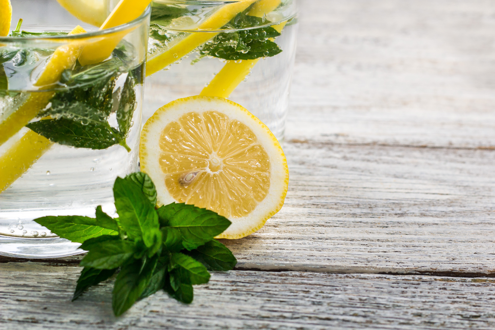 Two glasses of lemonade with lemon, mint and ice cubes on wooden background. Summer drink