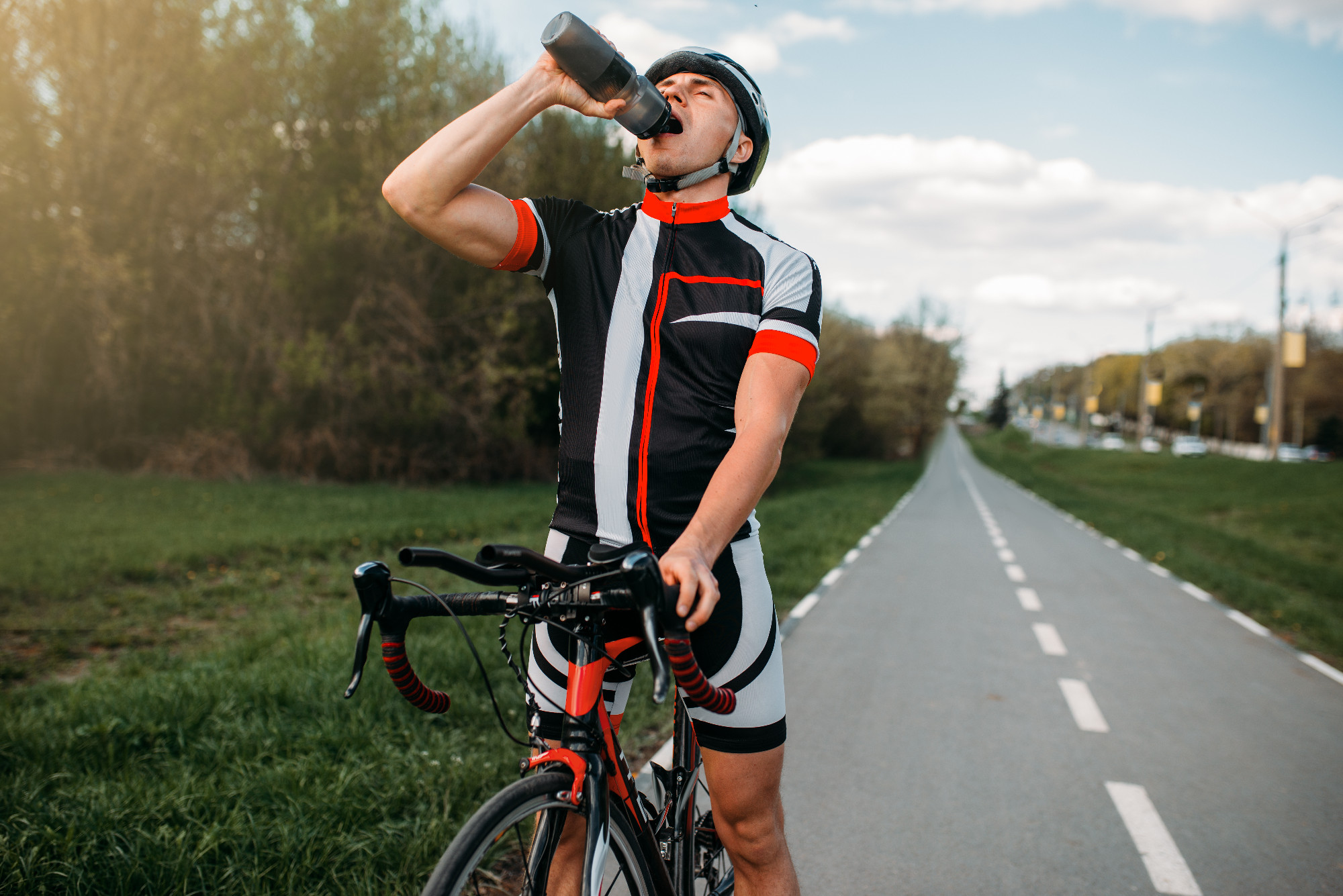 Male bycyclist drinks water while training