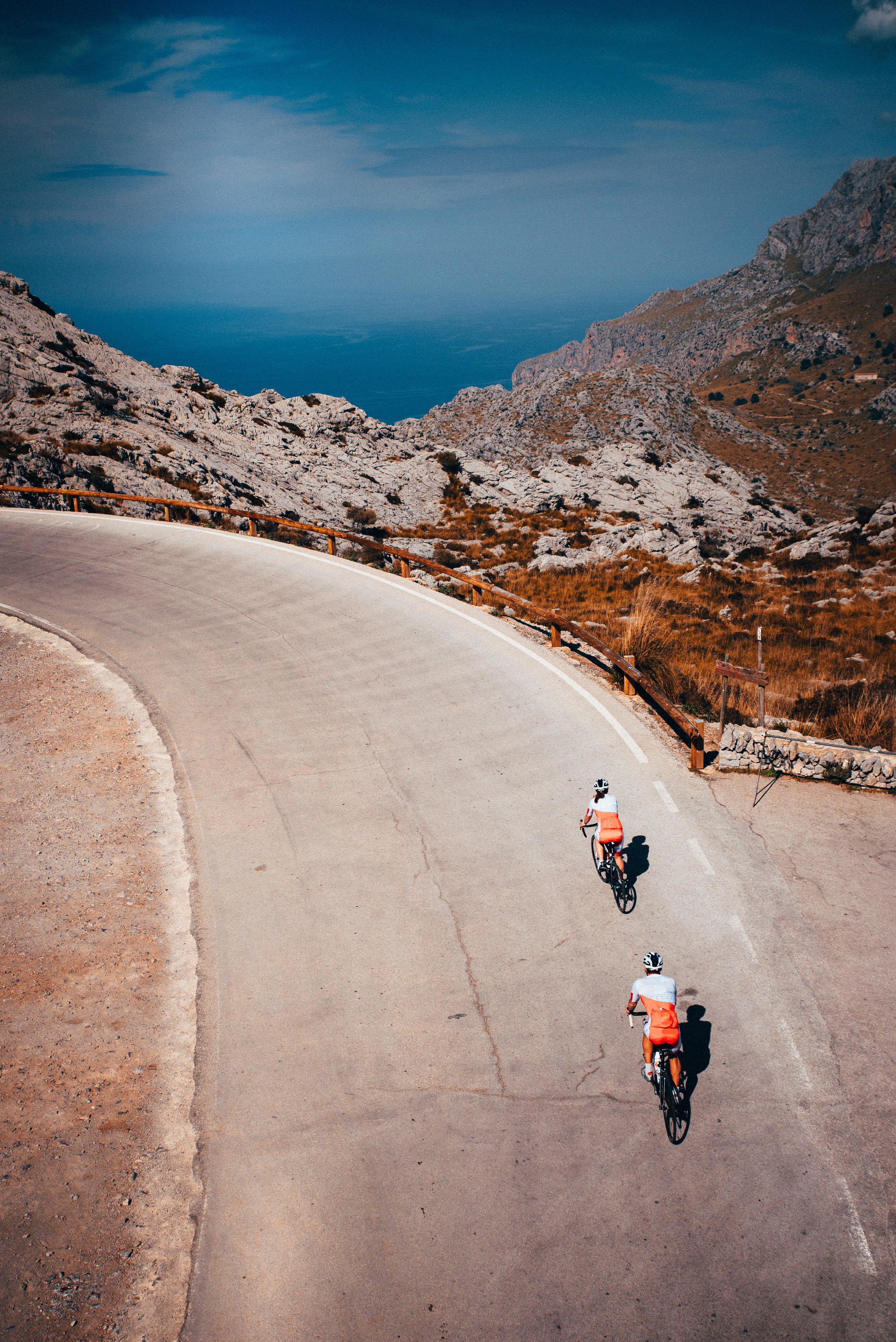 Couple ride together on road bicycle in mountains. Sea in background. Mallorca, Spain