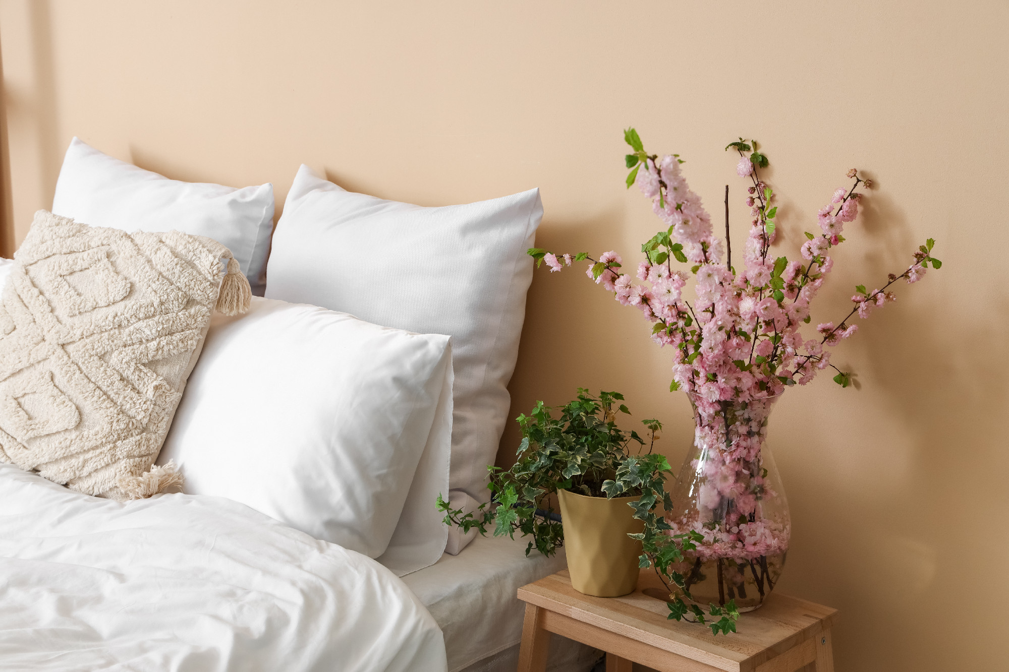 Vase with blooming sakura branches on step ladder near bed�