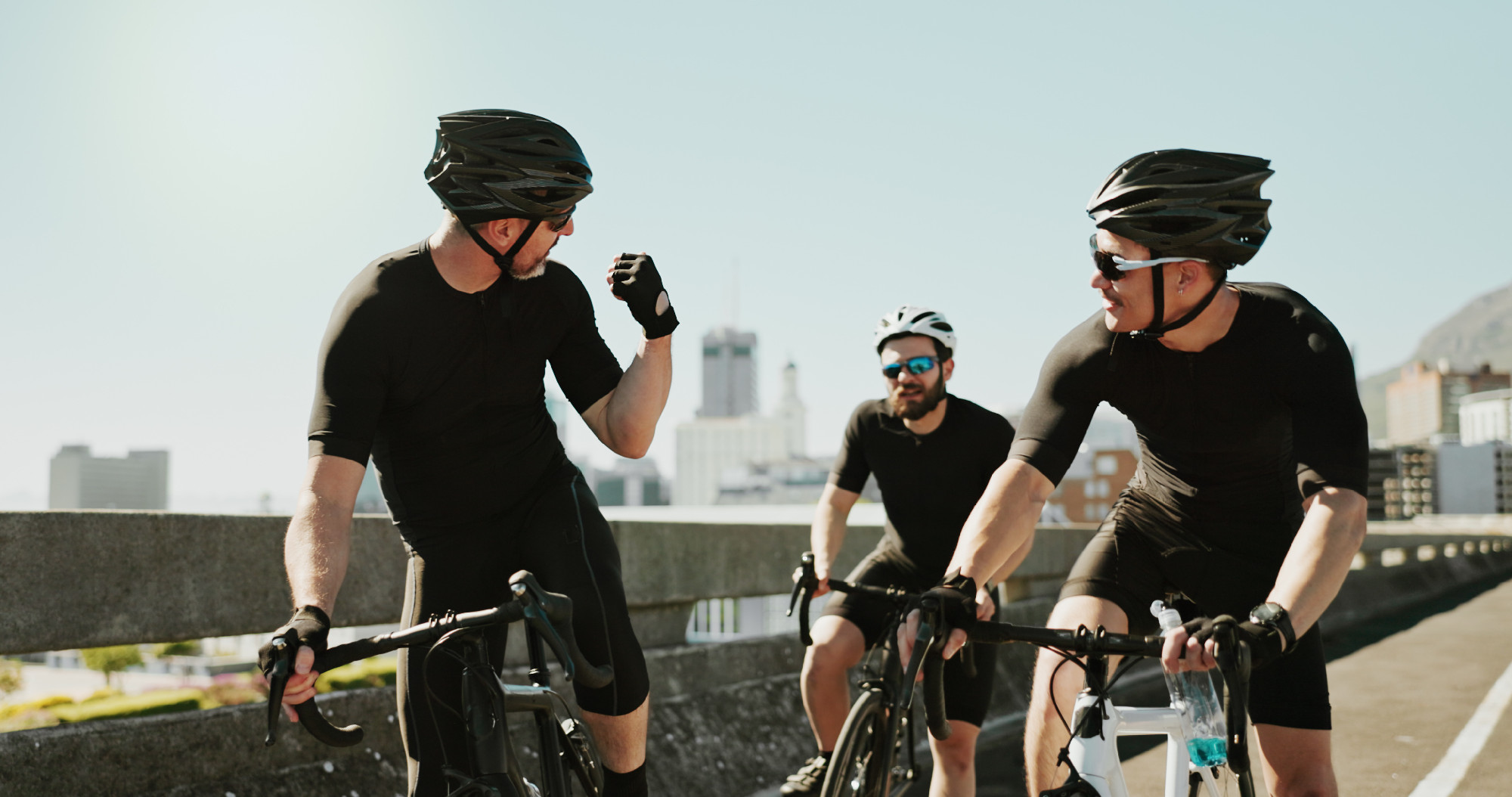 Bike, city and fist pump with sports people on bridge together for exercise or fitness motivation. Celebration, cycling and group of athlete friends outdoor in town for health or workout support