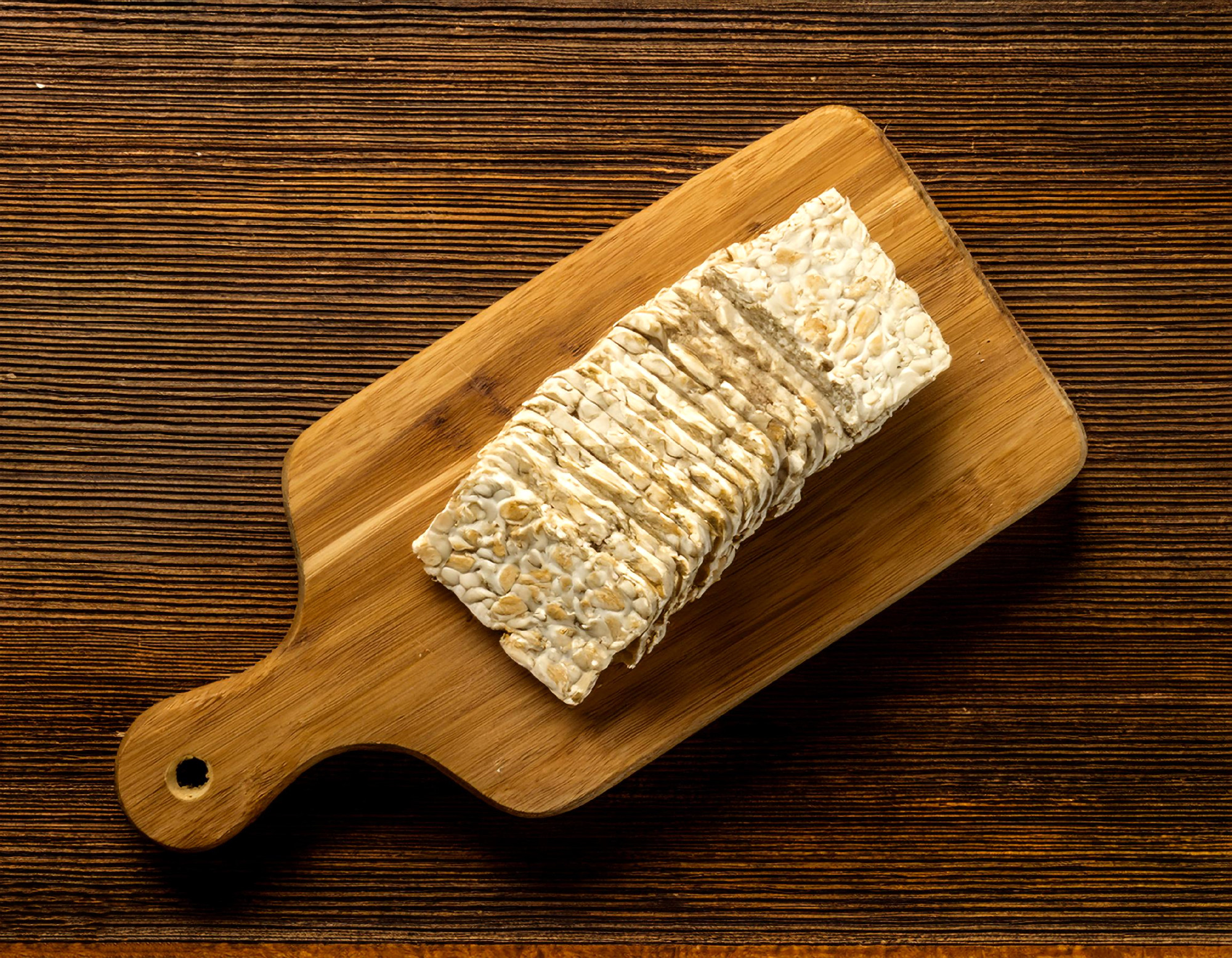Raw tempeh or tempe on a wooden cutting board, isolated against