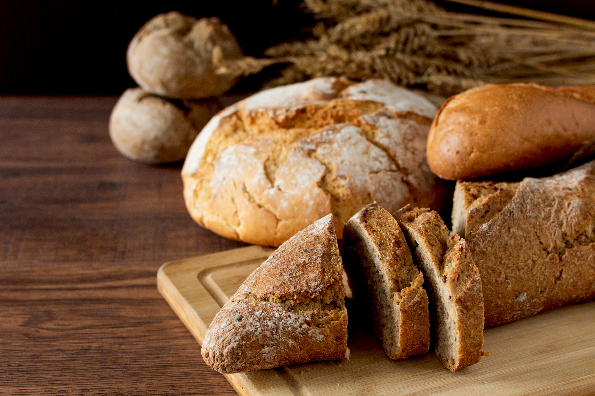 Loaf of bread sliced and other variety of bread on wooden table.