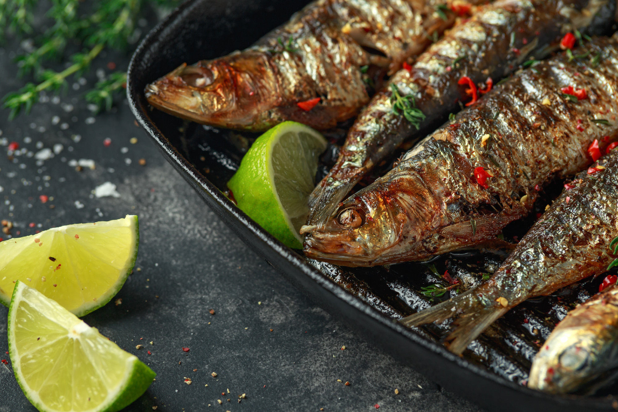 Grilled sardines with thyme, chili and lime wedges on cast iron skillet