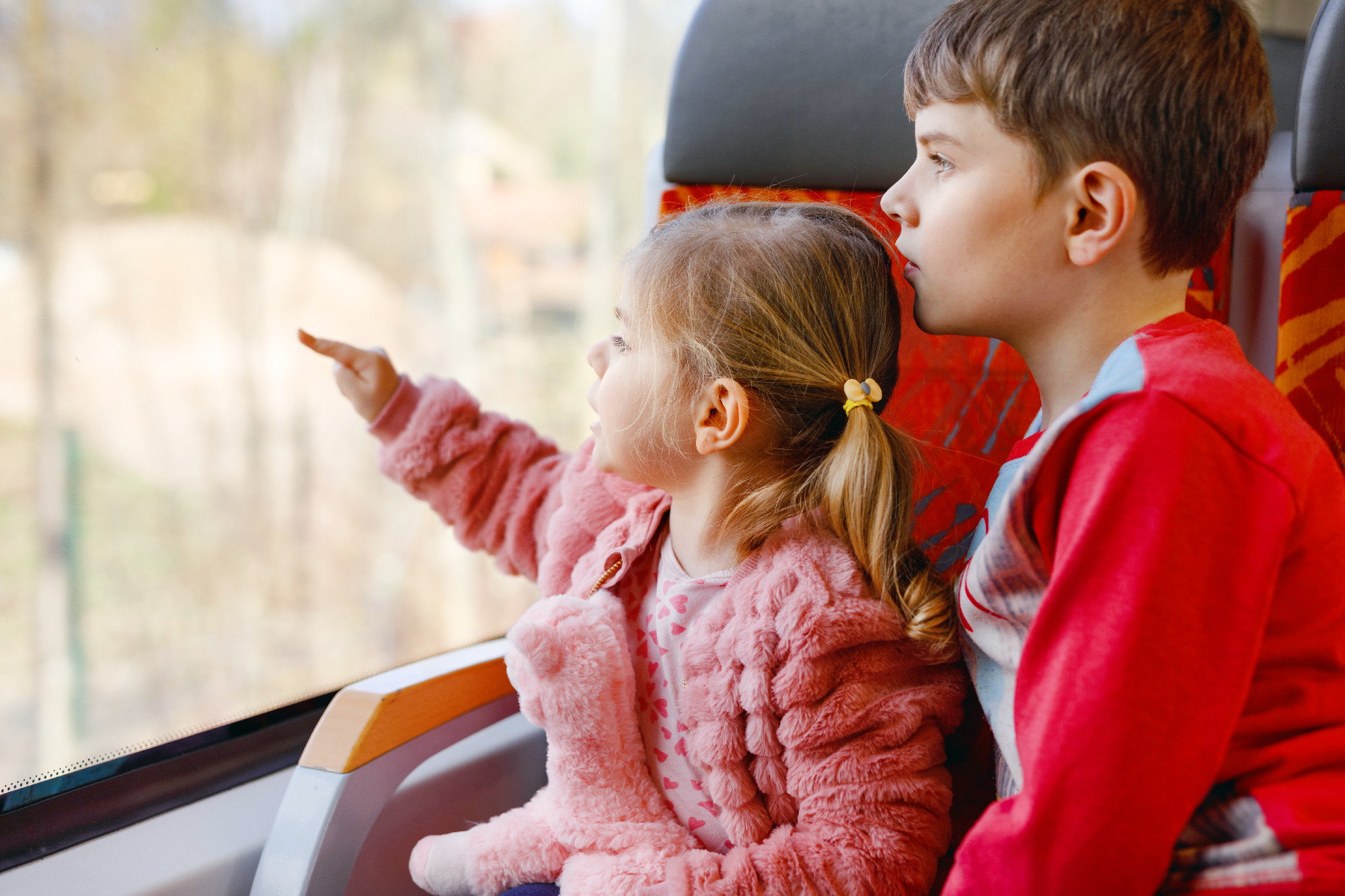 Cute little toddler girl and brother kid boy sitting in train and looking out of window. Two adorable happy healthy children having fun together. Smiling siblings going on family vacations by railroad