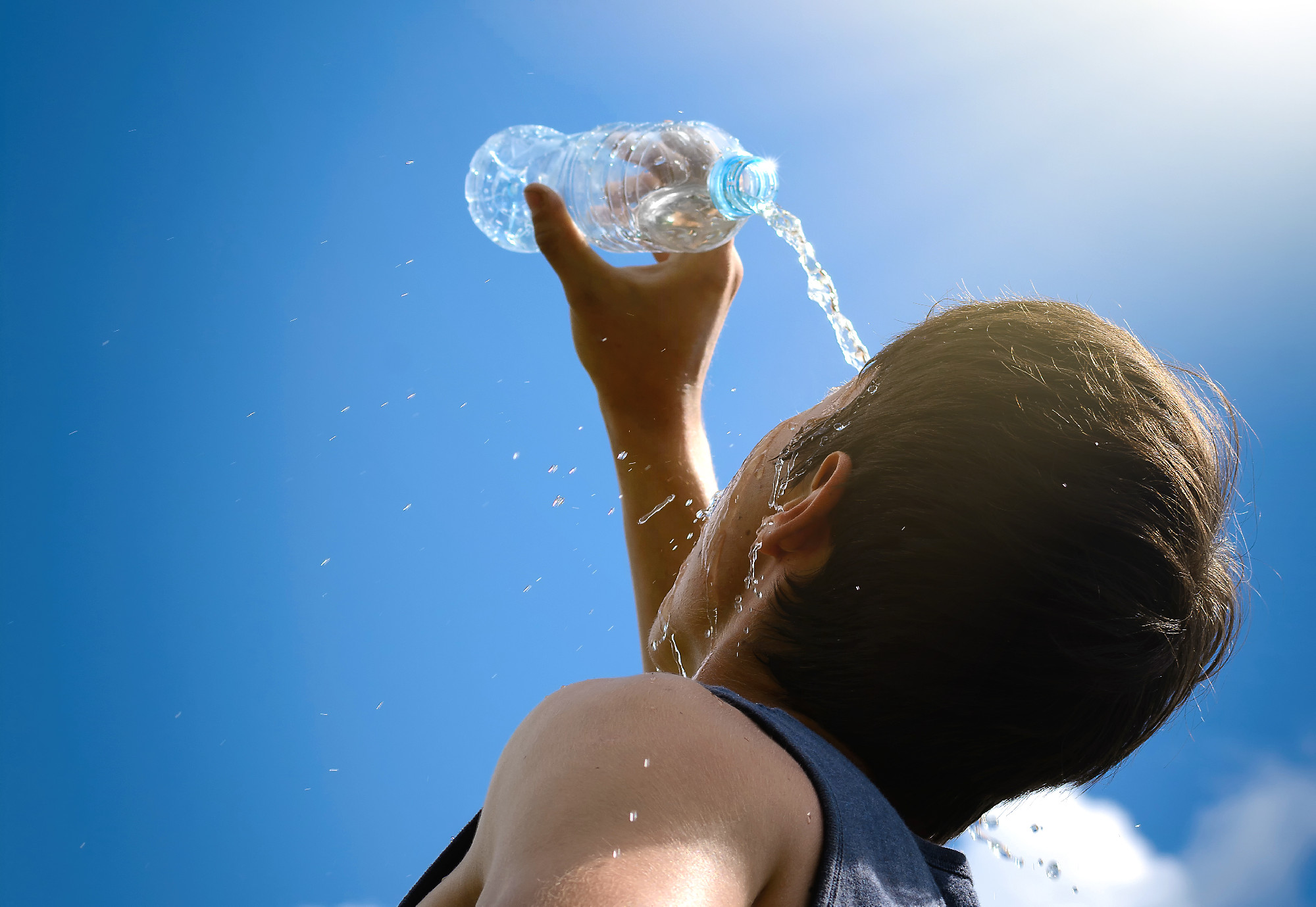Young man splashing and pouring fresh water from a bottle on his face.