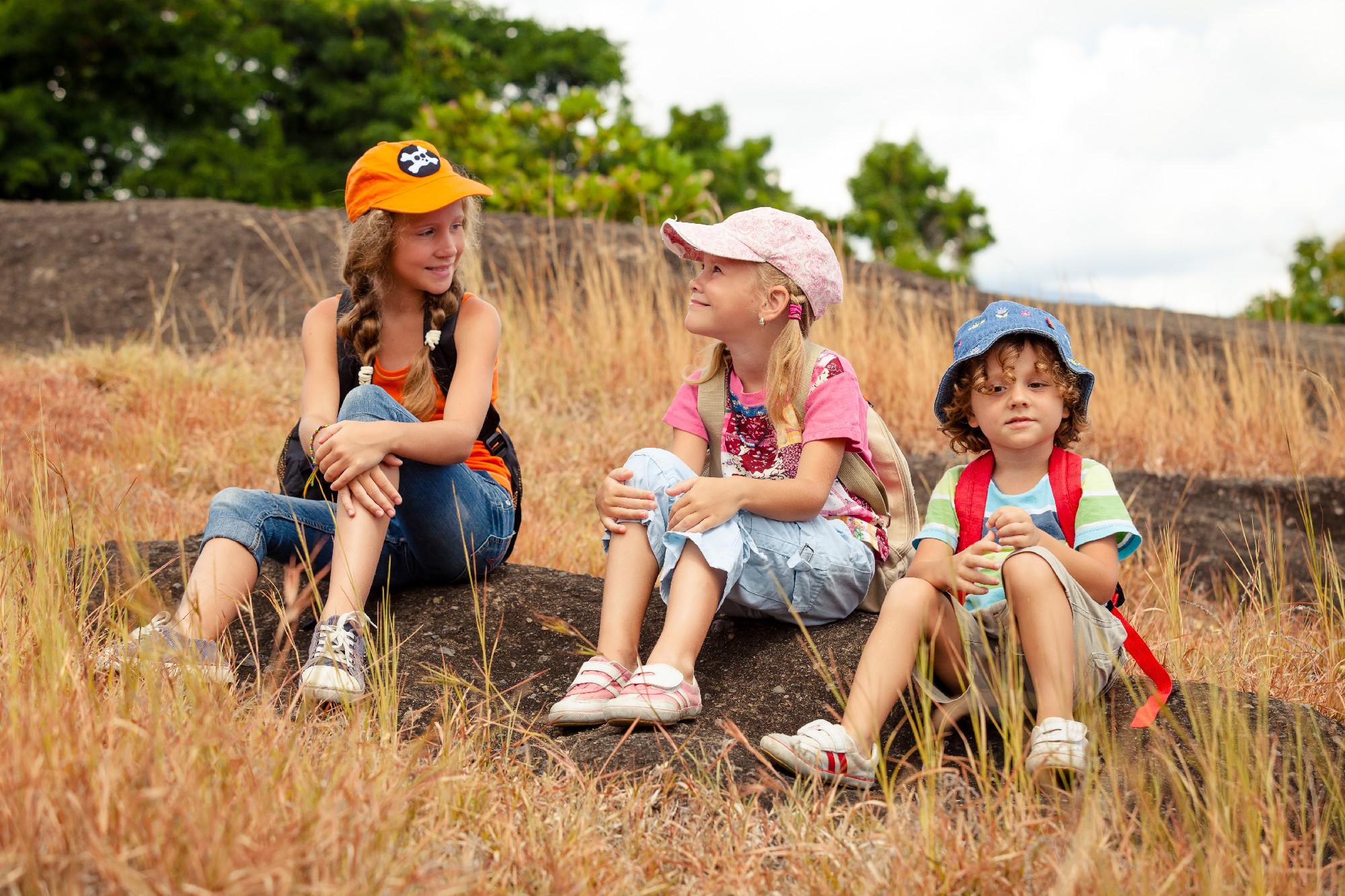 three little kids with backpack sitting on the footpath in the m