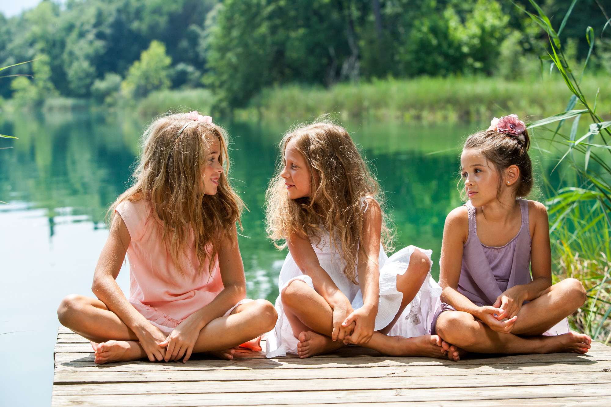 Three girl friends sitting on jetty at lake.