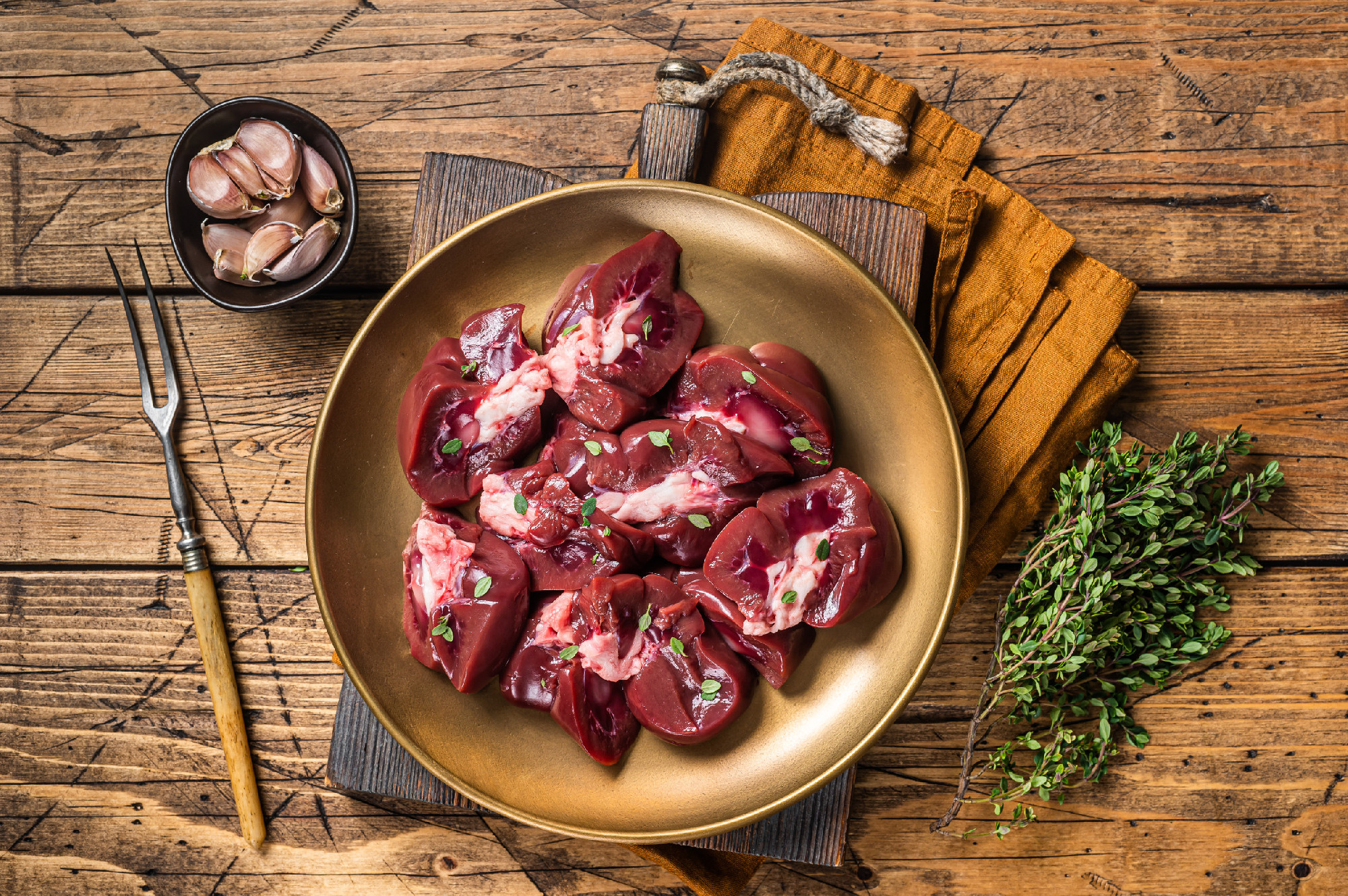 Lamb kidney, raw sliced offal on plate with thyme. Wooden background. Top view