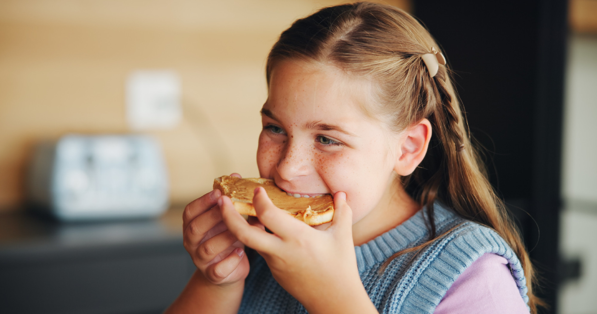 Eating, happy and child with toast in morning for breakfast in home for nutrition, diet or vitamins. Hungry, food and girl kid enjoying bread with peanut butter for snack, lunch or meal at house.