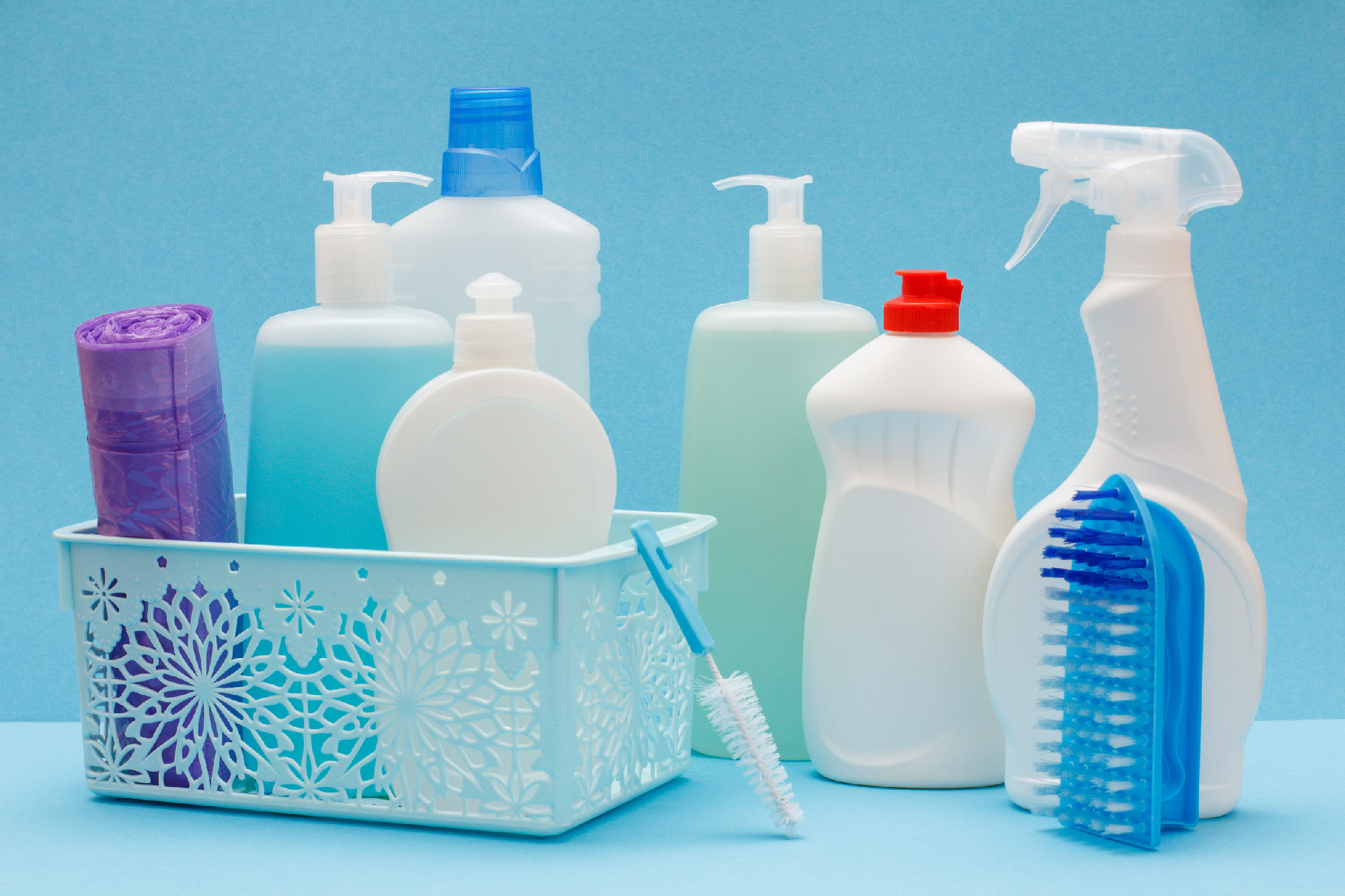 Bottles of dishwashing liquid in basket, sponges and brushes on blue background.