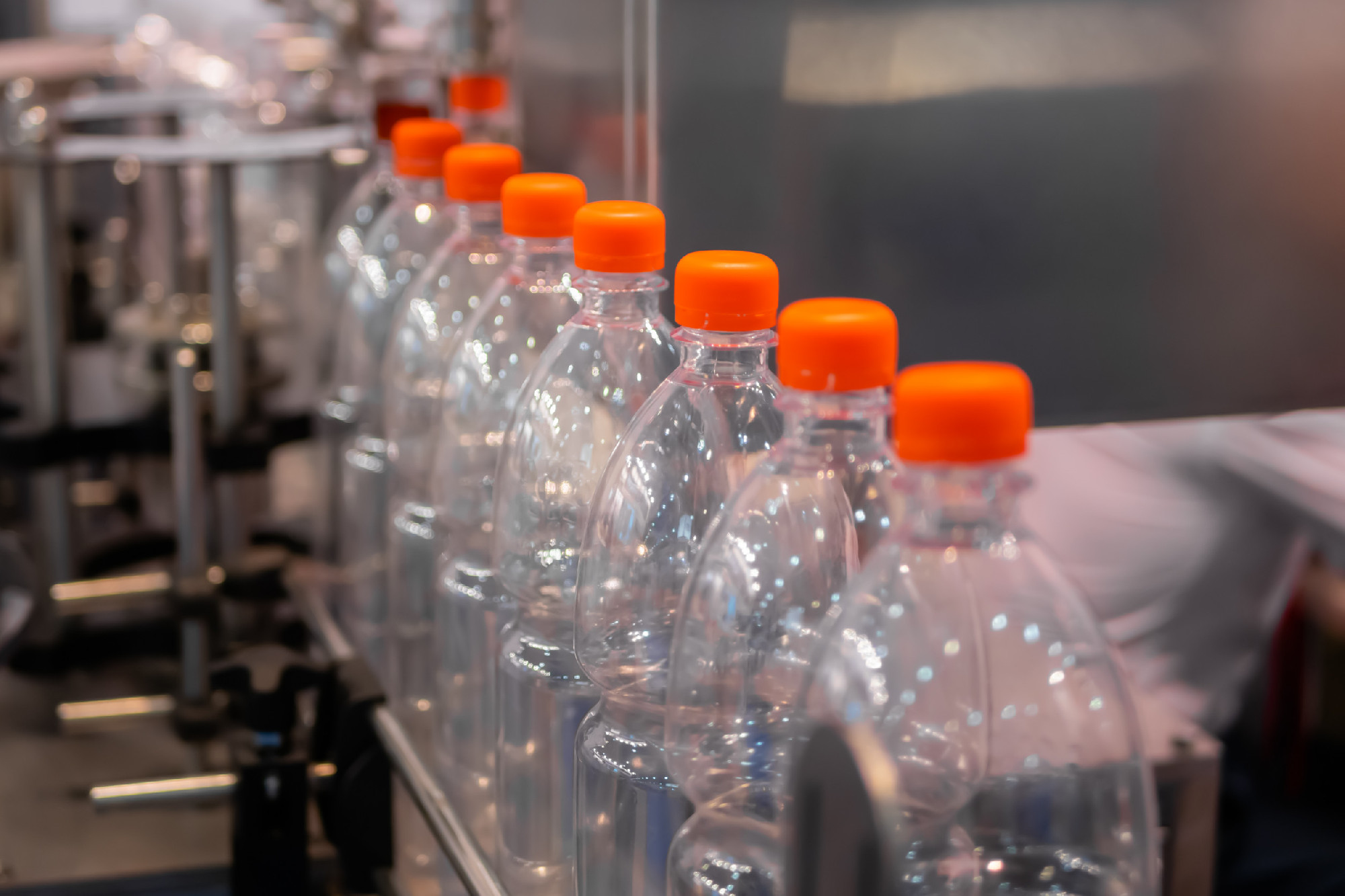 Row of empty pet lemonade bottles with orange caps on conveyor belt - close up