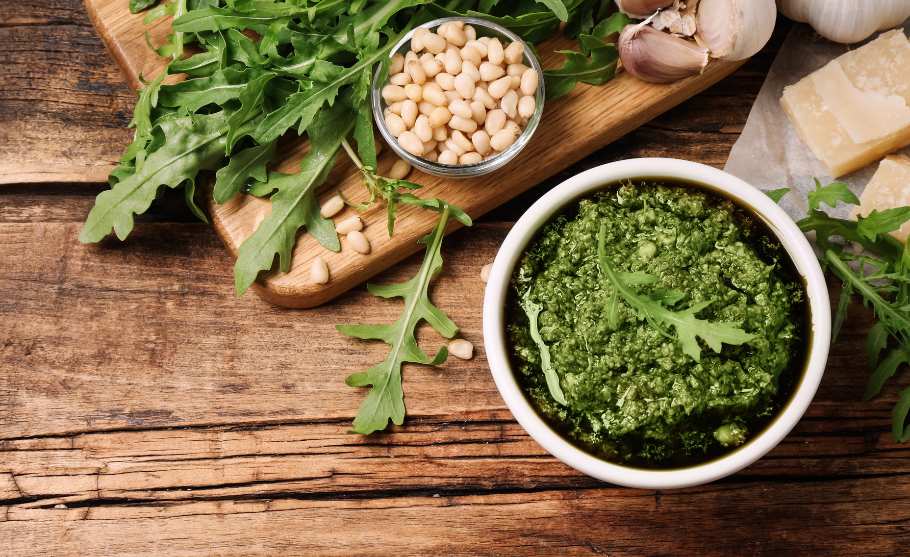 Bowl of tasty arugula pesto and ingredients on wooden table, fla