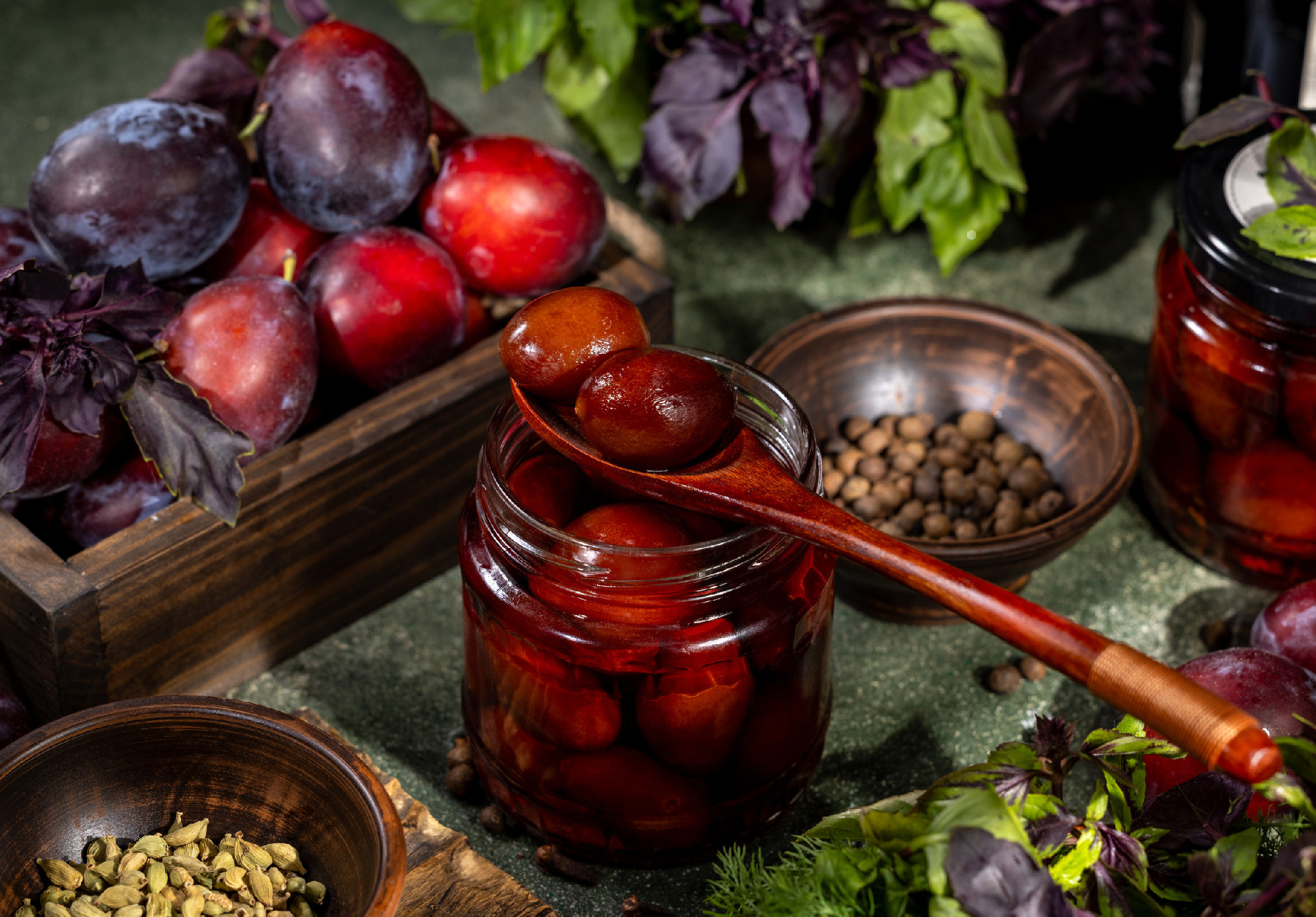 Pickled plums preserved in glass jar with fresh plums, herbs, and spices