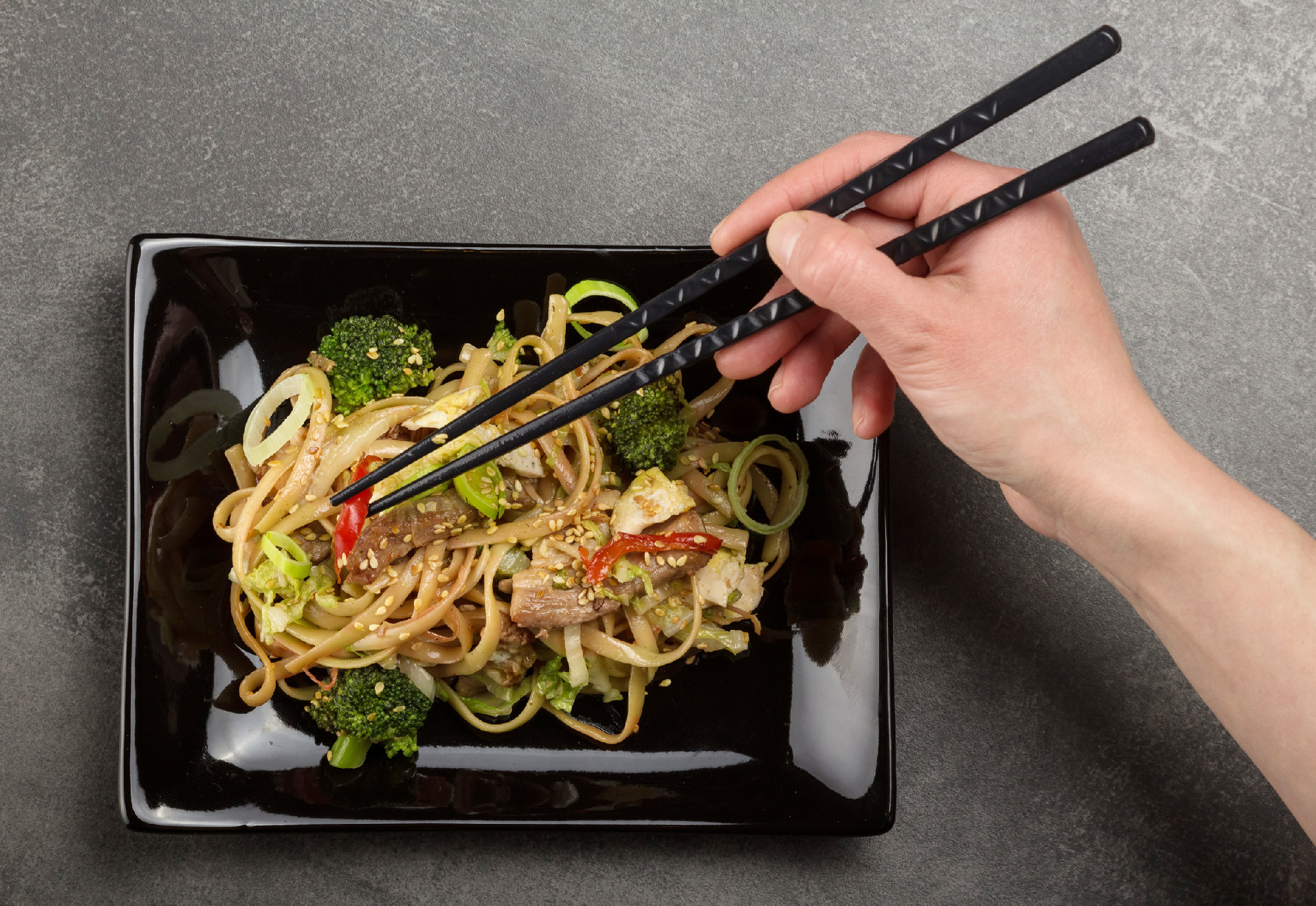 Spicy Asian dish, noodles with meat and vegetables with sesame, on black plate