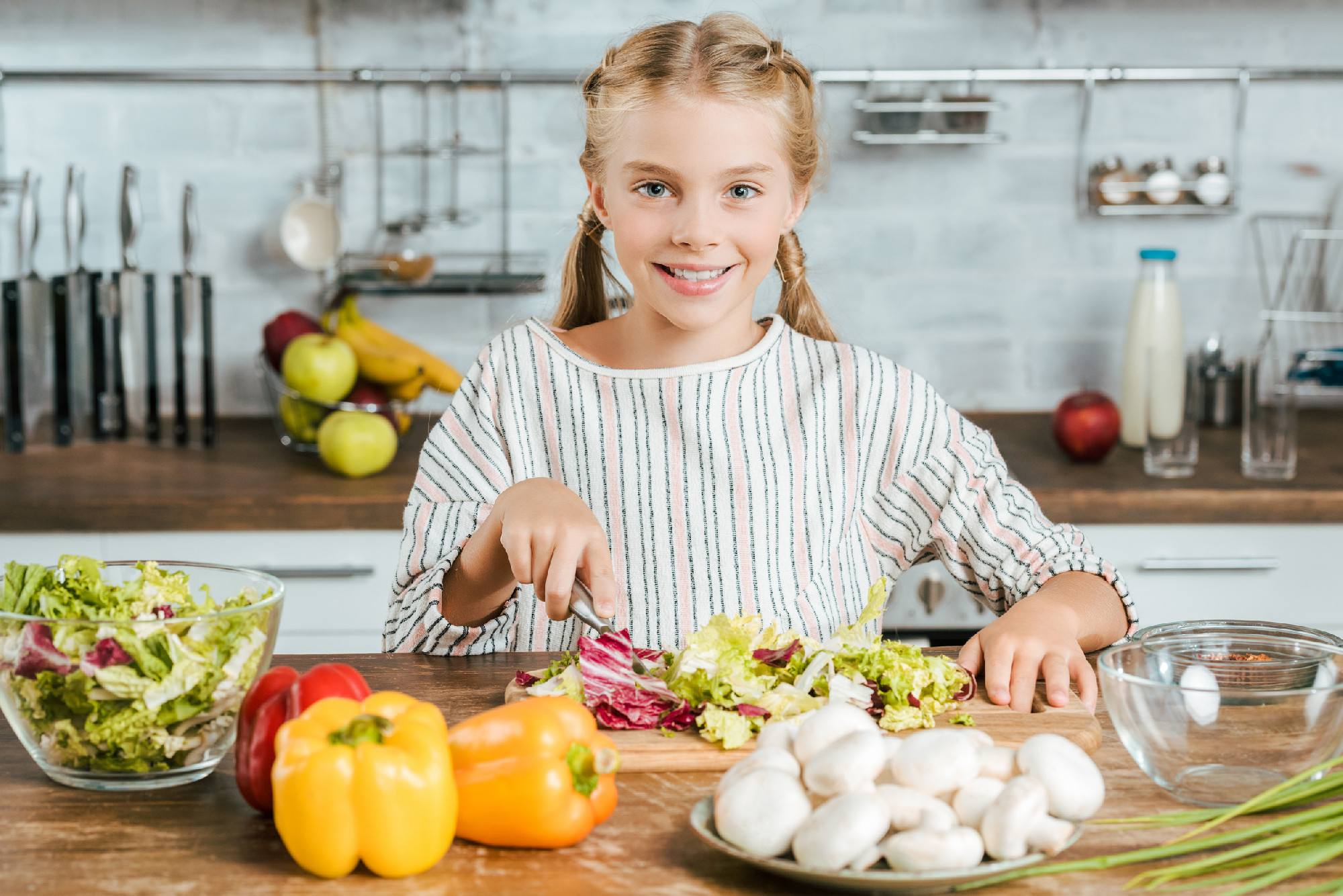 happy little child cutting lettuce for salad at kitchen and looking at camera