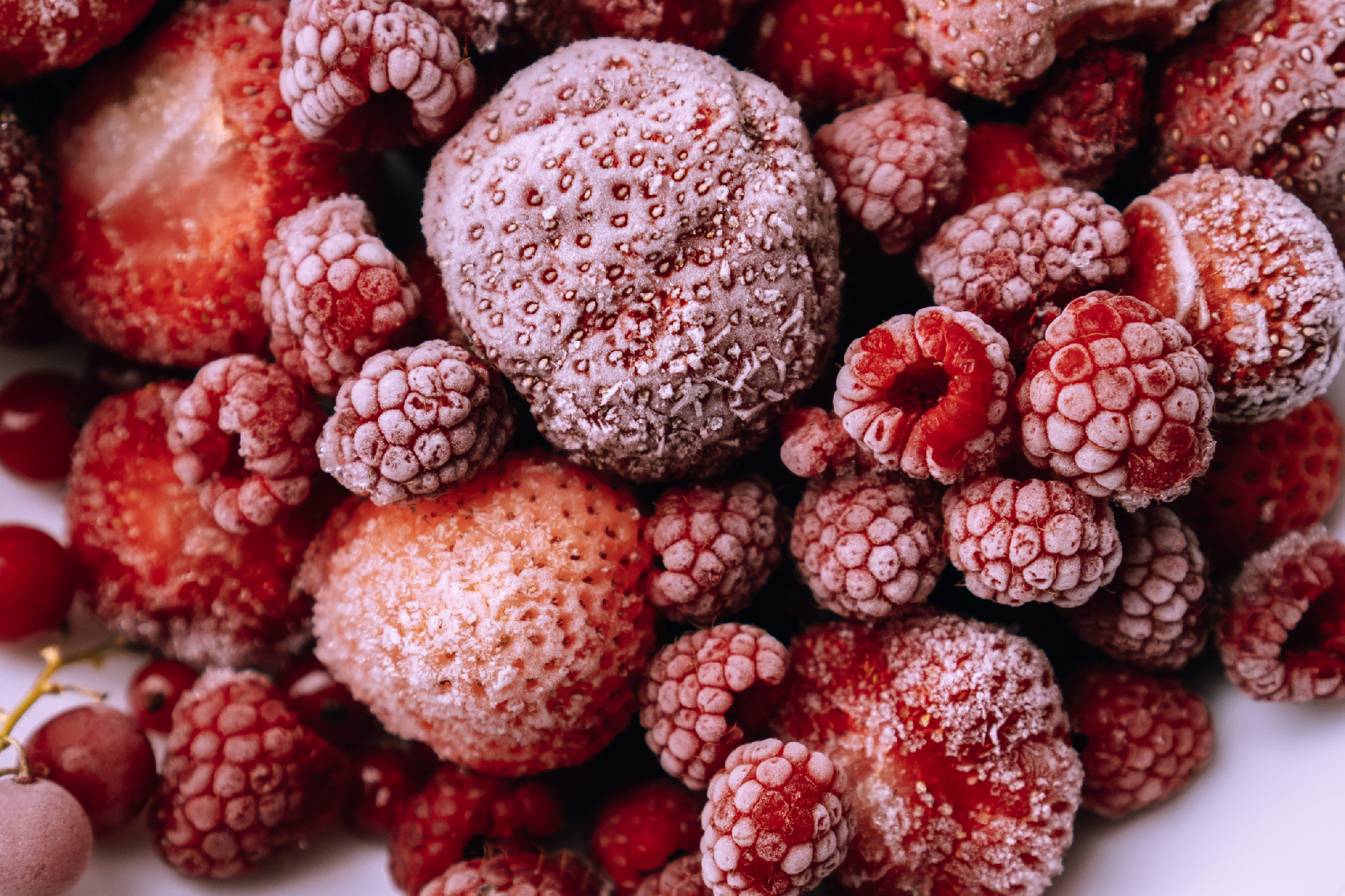 Red frozen berries covered with frost on white plate. Raspberries, strawberries, red currants. Preservation of vitamins