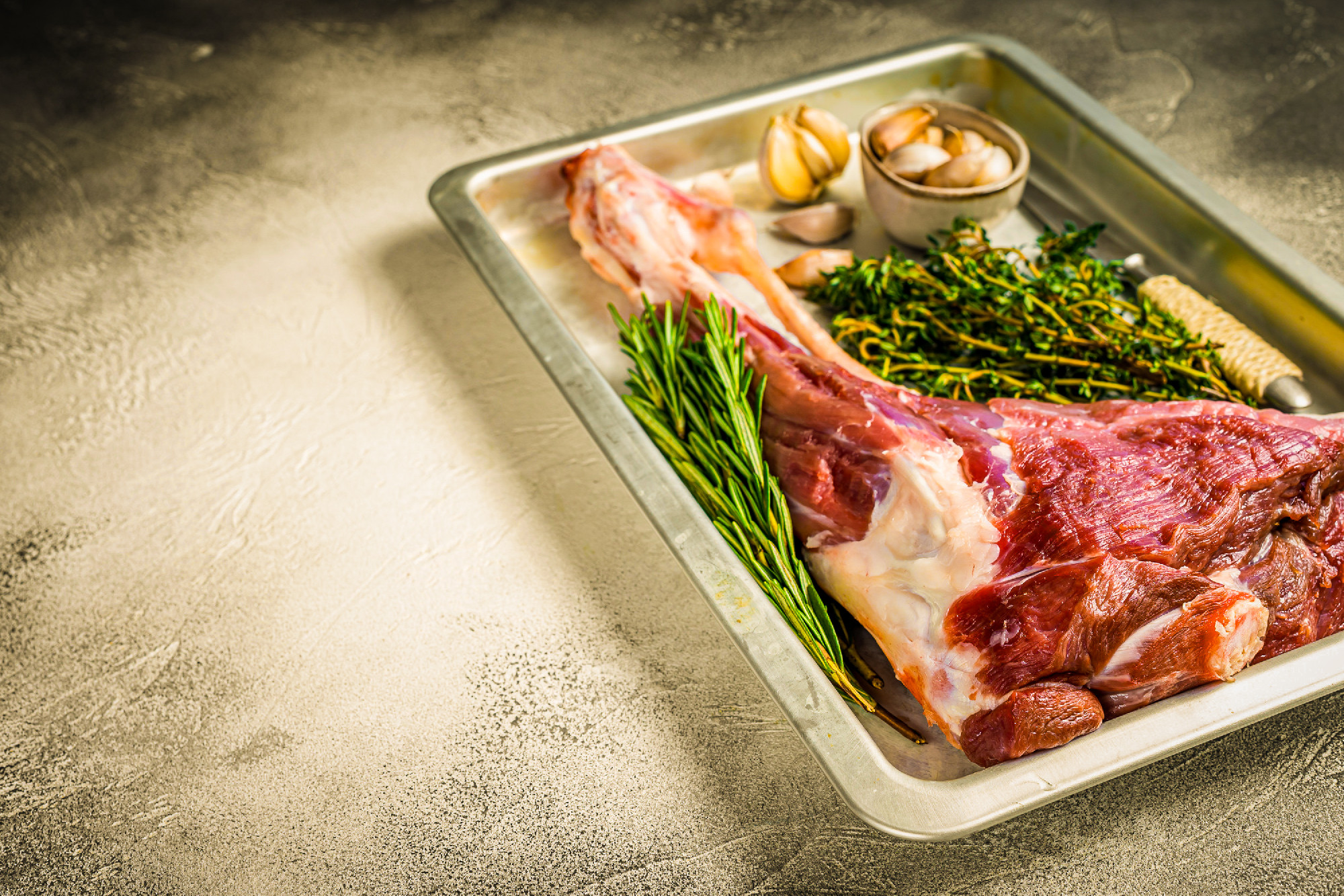 Uncooked Raw goat or lamb leg with herbs in baking tray. White b