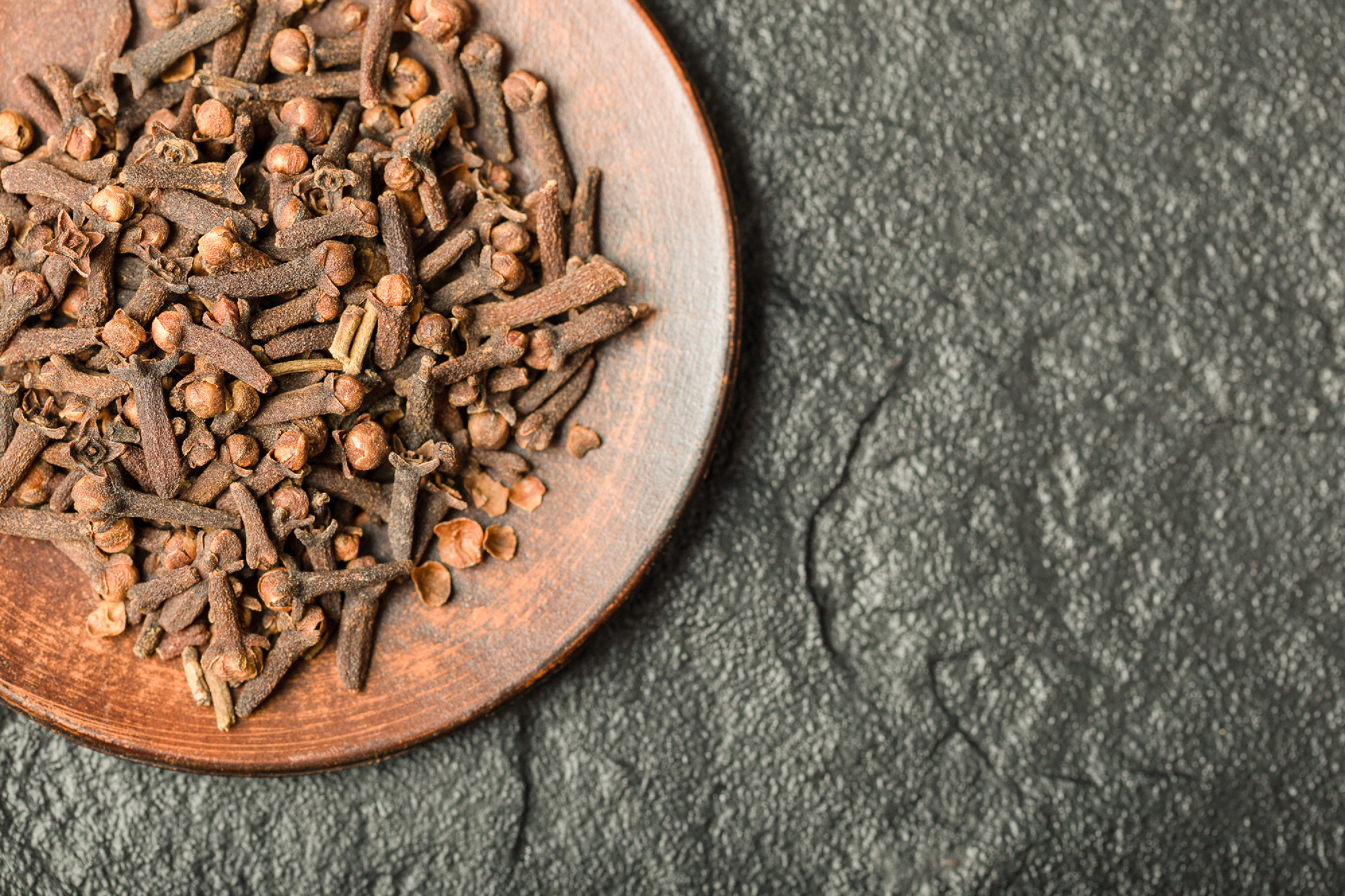 A brown plate full of dried cloves on a dark background