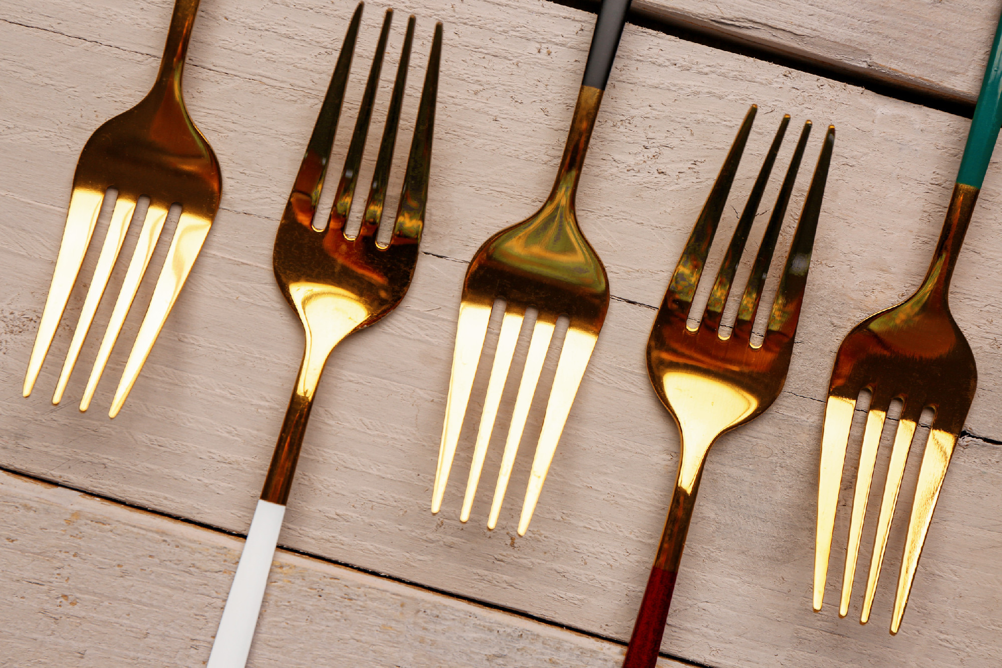 Golden forks with colored handles on grey wooden background�