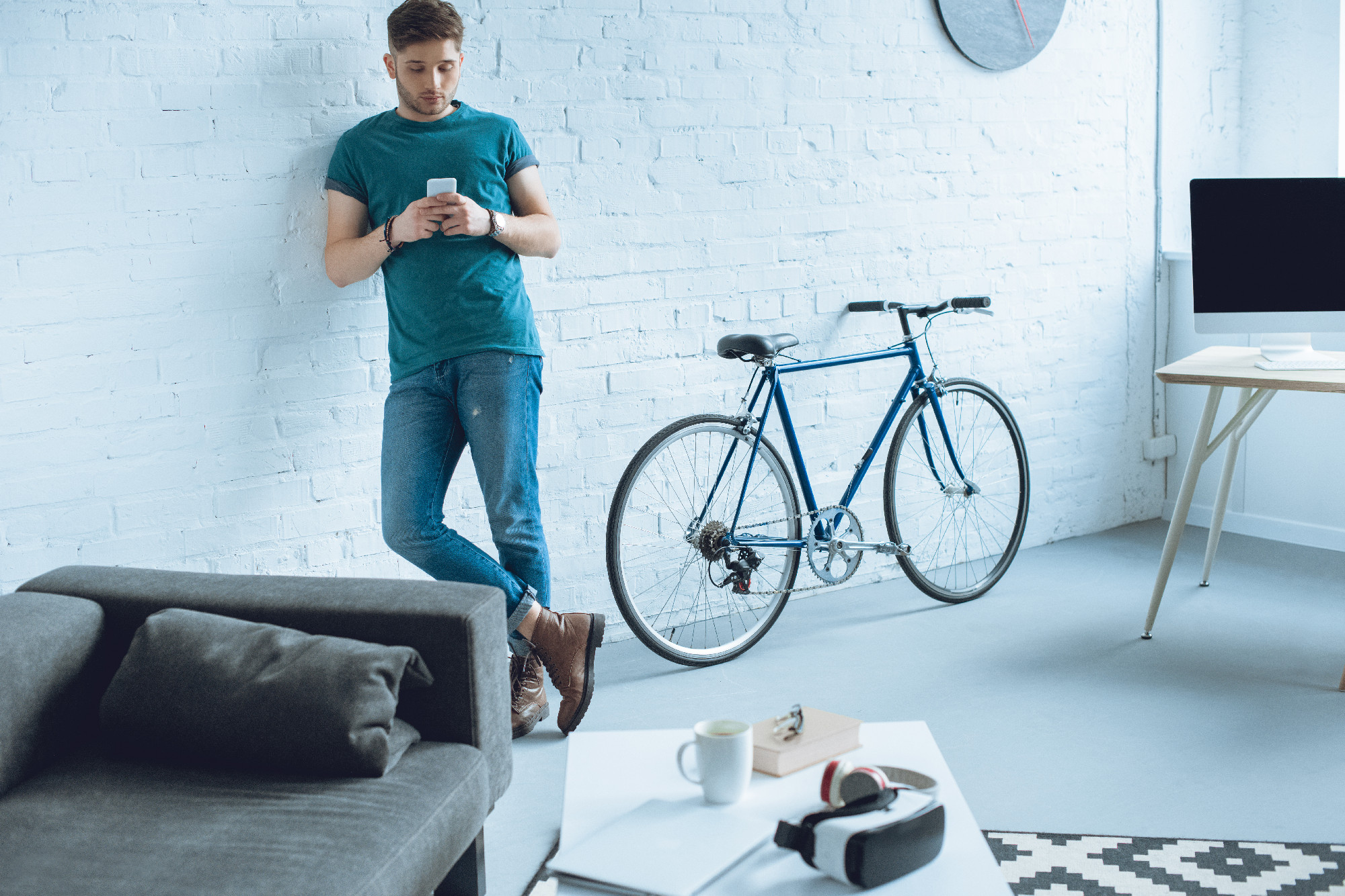 handsome young man leaning at wall and using smartphone at home