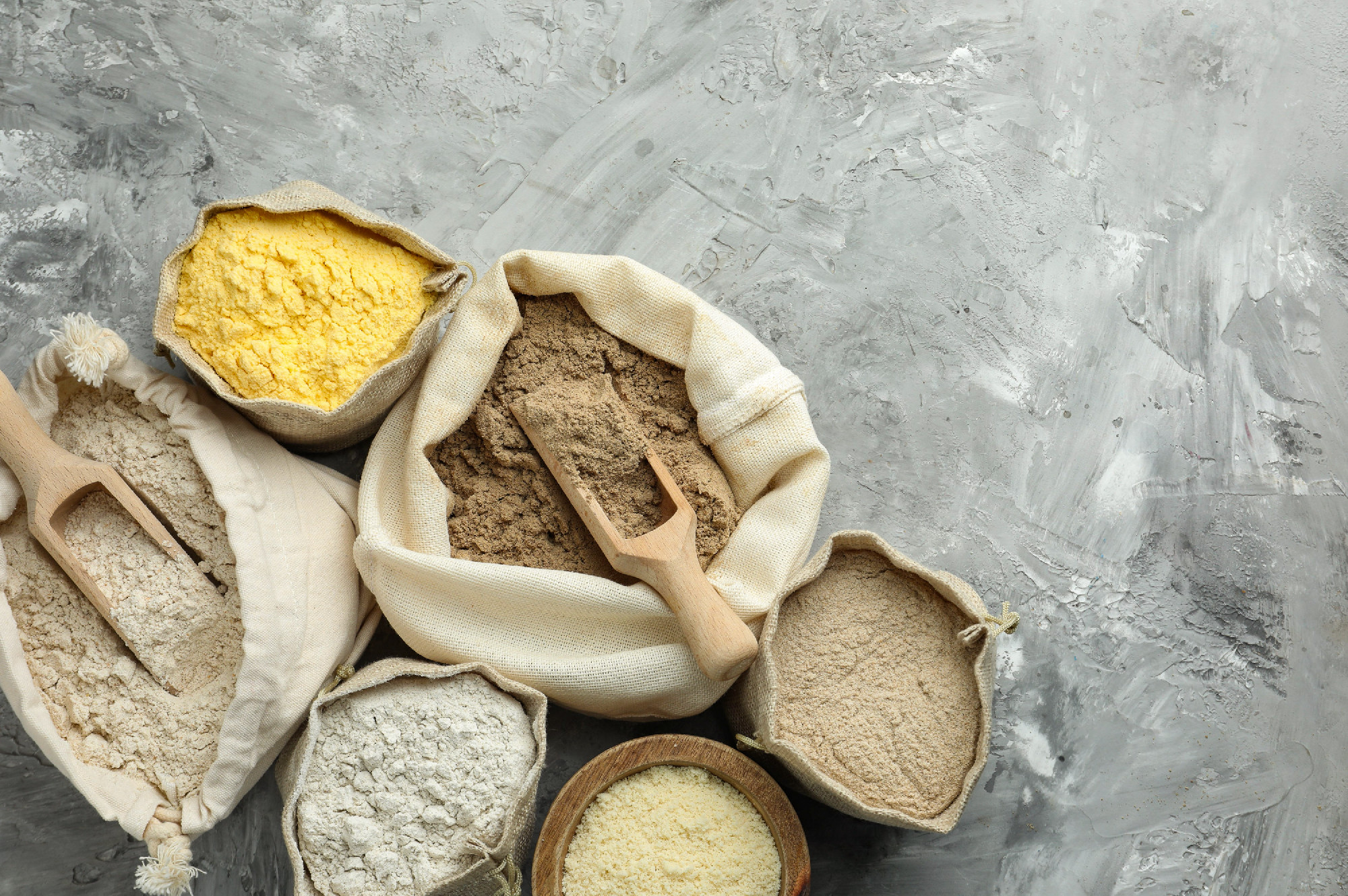 Different types of flour in bags on grey textured table, flat la