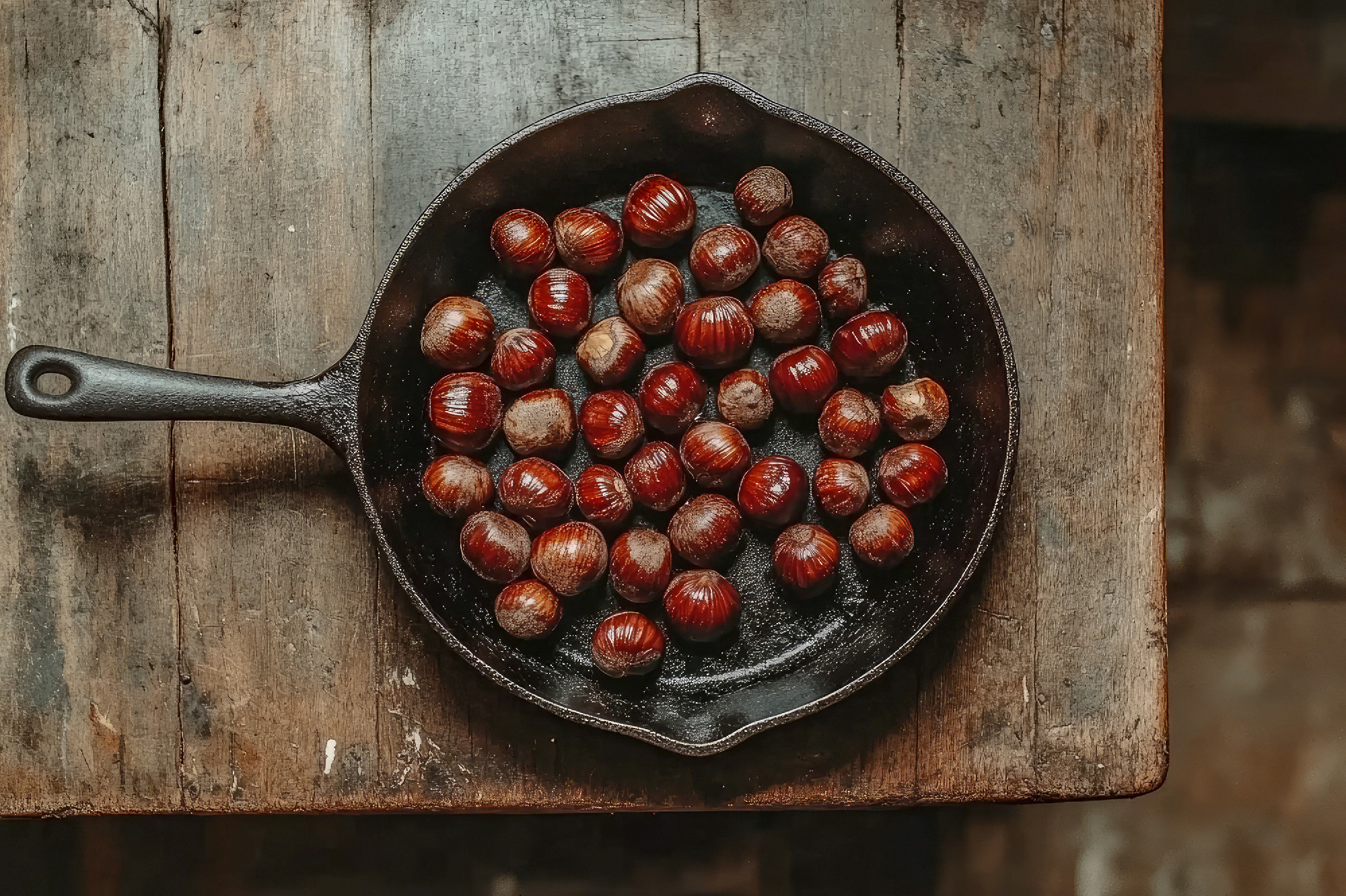 Cast iron skillet filled with roasted chestnuts on rustic wooden