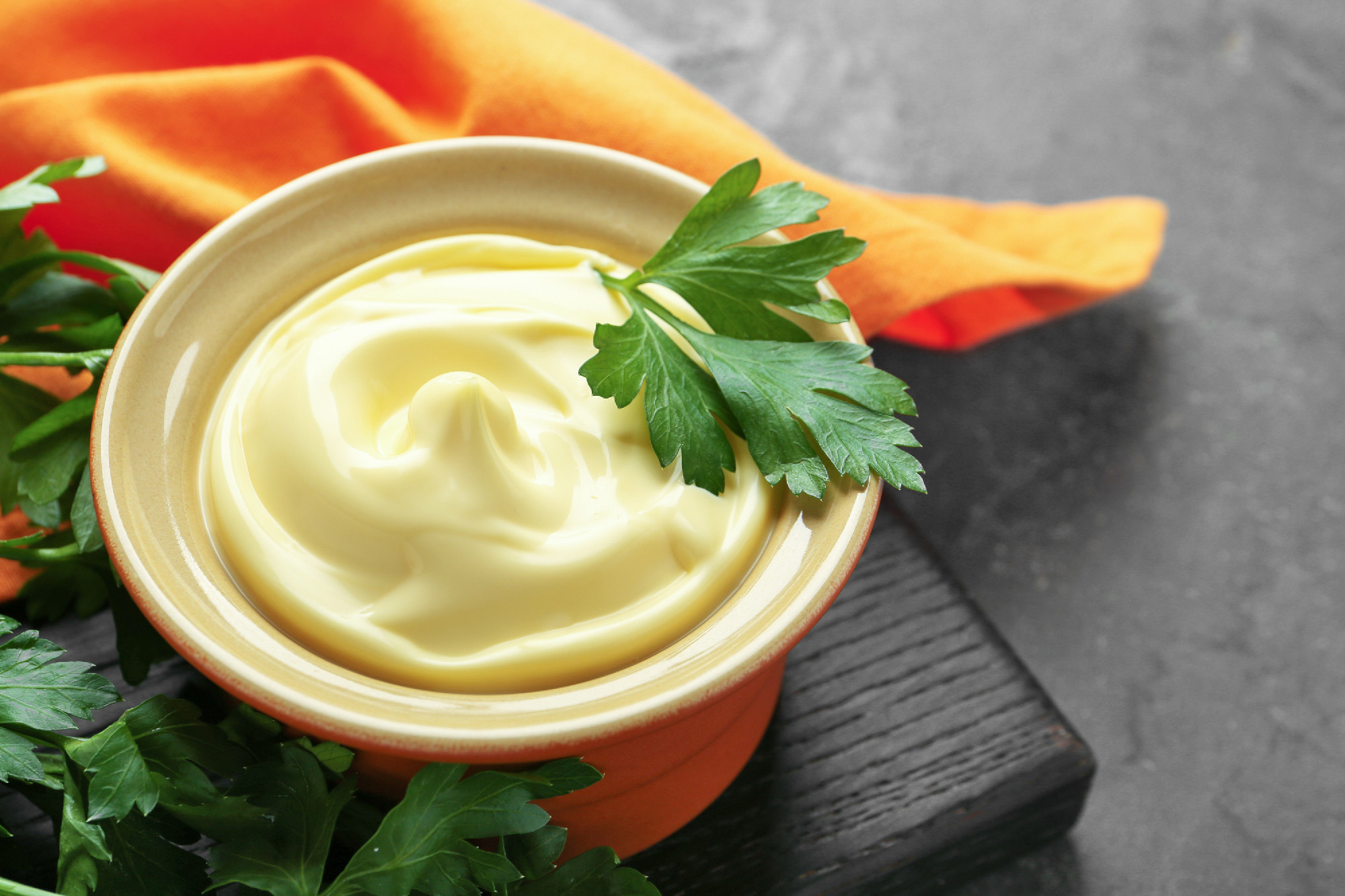 Delicious mayonnaise sauce in bowl with parsley on grey table, c