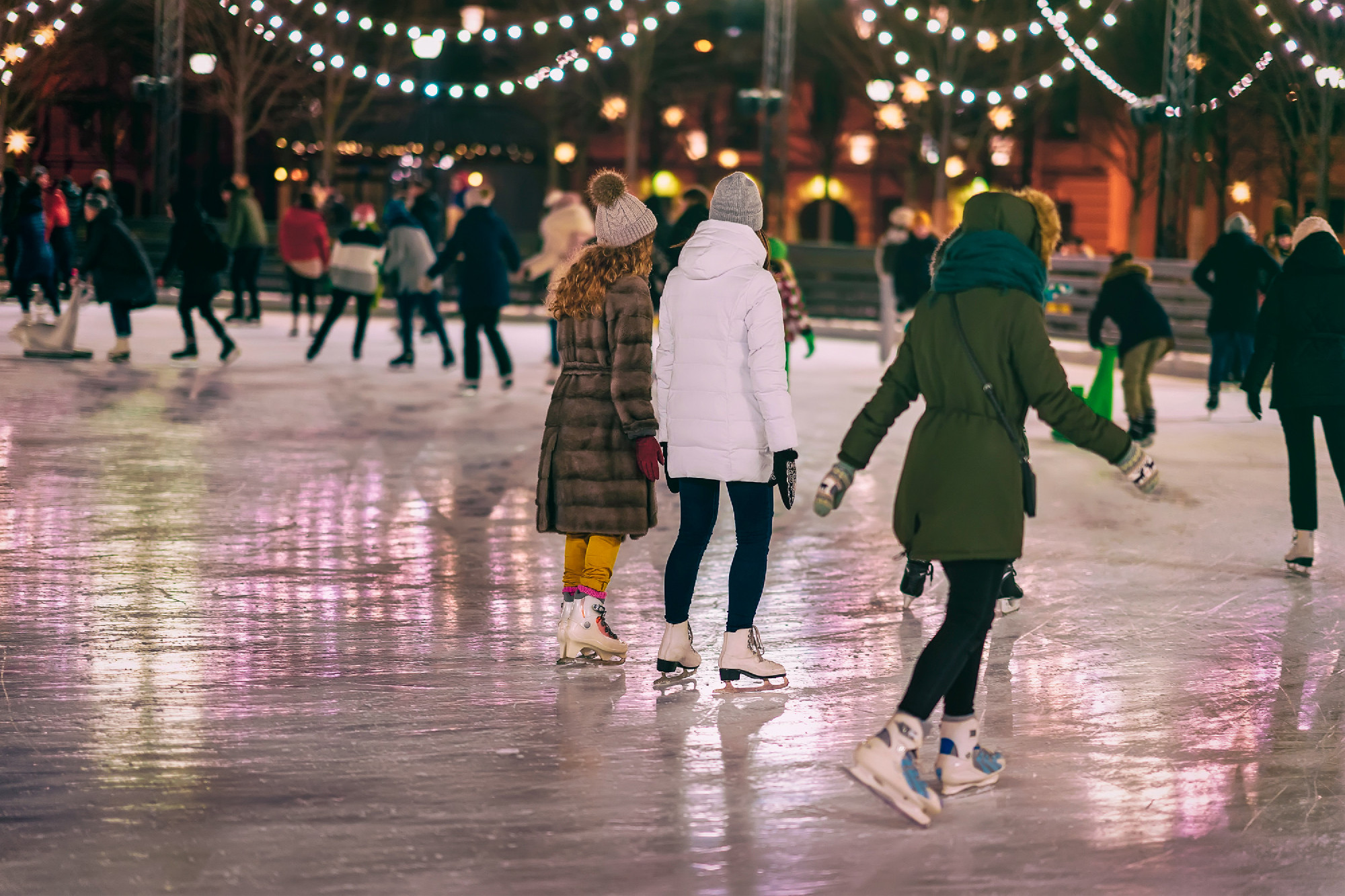 Group of girs skating back to us. Girlfriends ice skating in cit