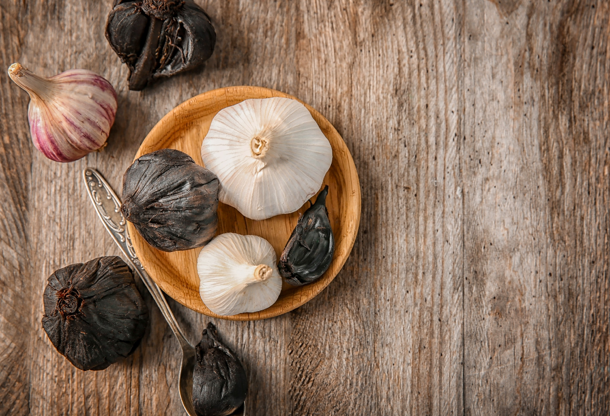Plate with black (Allium sativum) and white garlic bulbs on wood