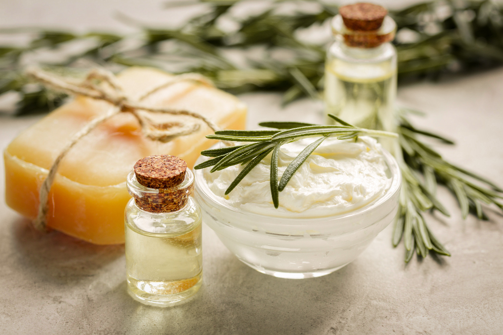 homemade cosmetics with rosemary herbs on white stone background