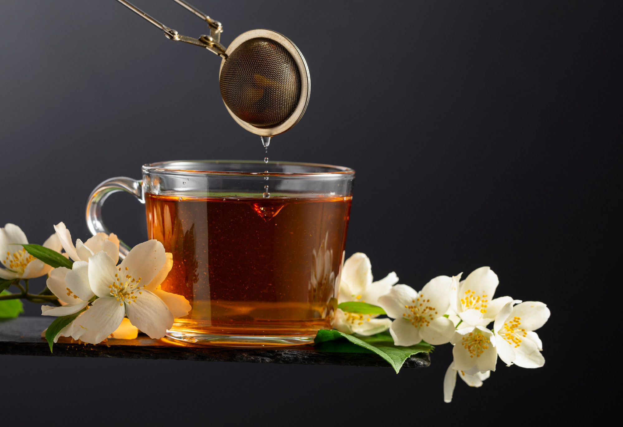 Cup of jasmine tea and fresh jasmine flowers on a black backgrou