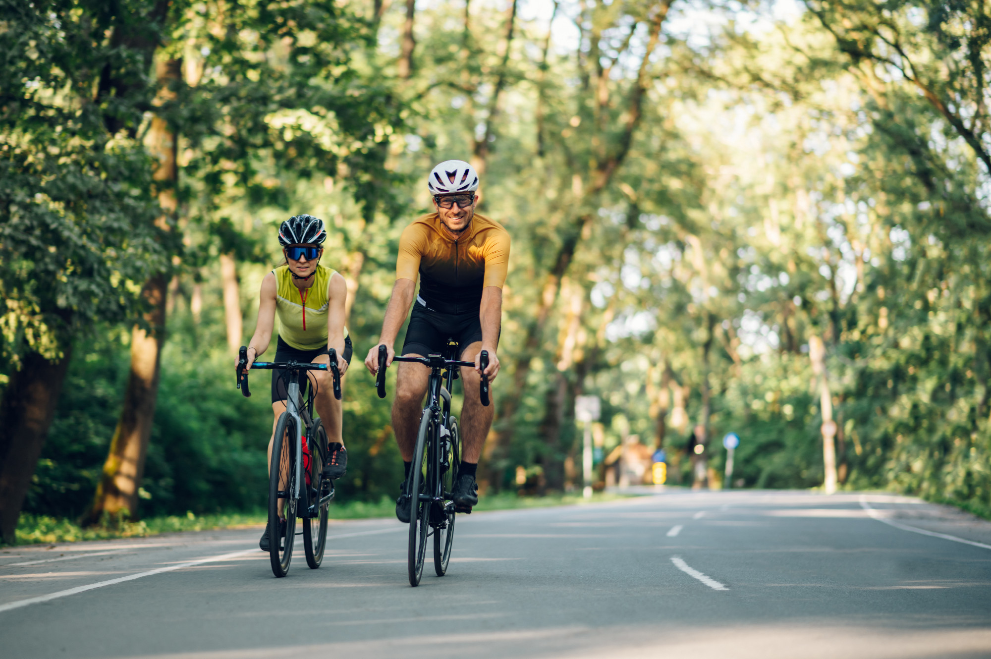 Couple riding road bicycles outside and wearing helmets and sung