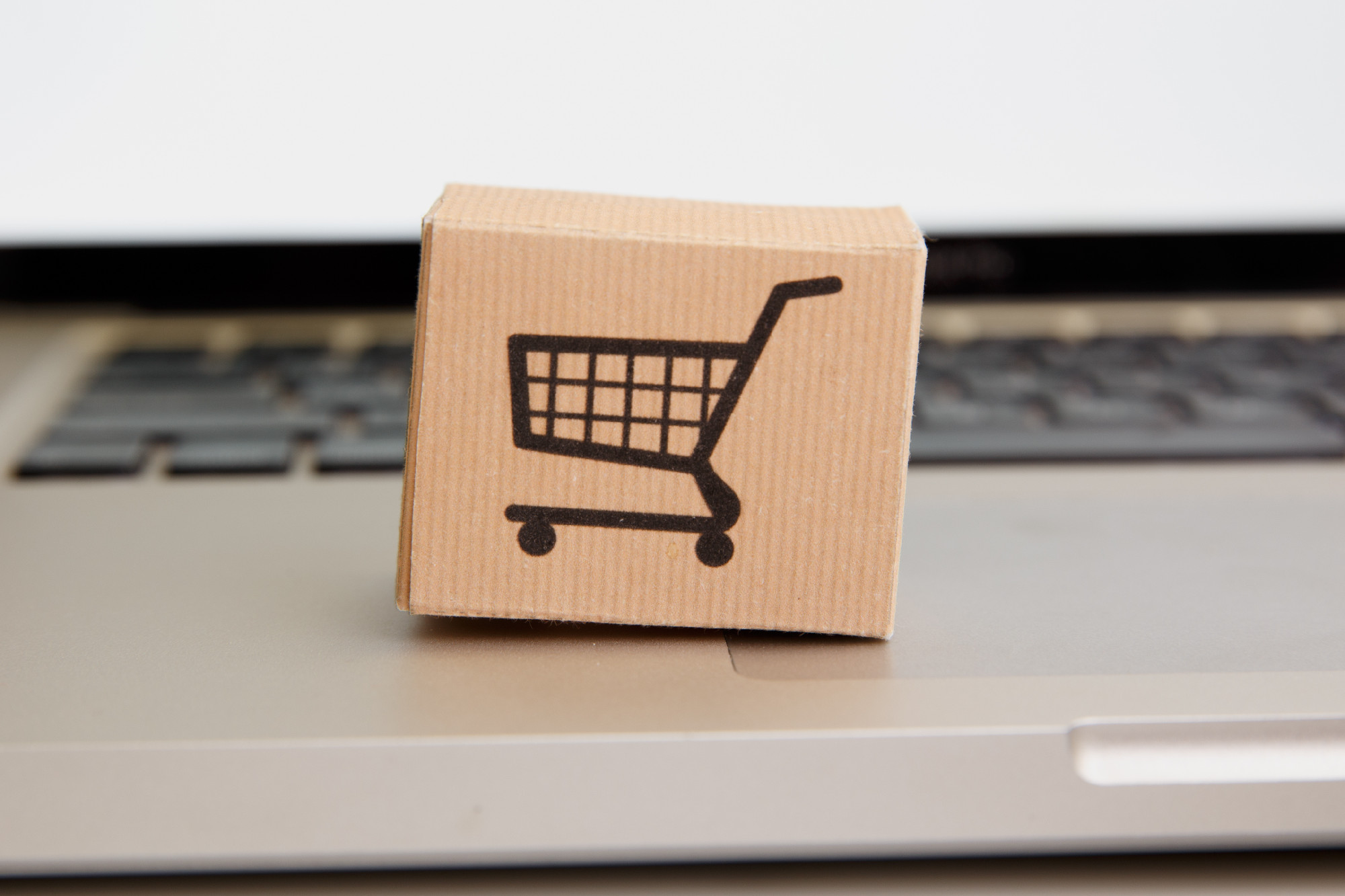 Online shopping . ecommerce and delivery service concept : Paper cartons with a cart or trolley logo on a laptop keyboard, depicts customers order things from retailer sites via the internet