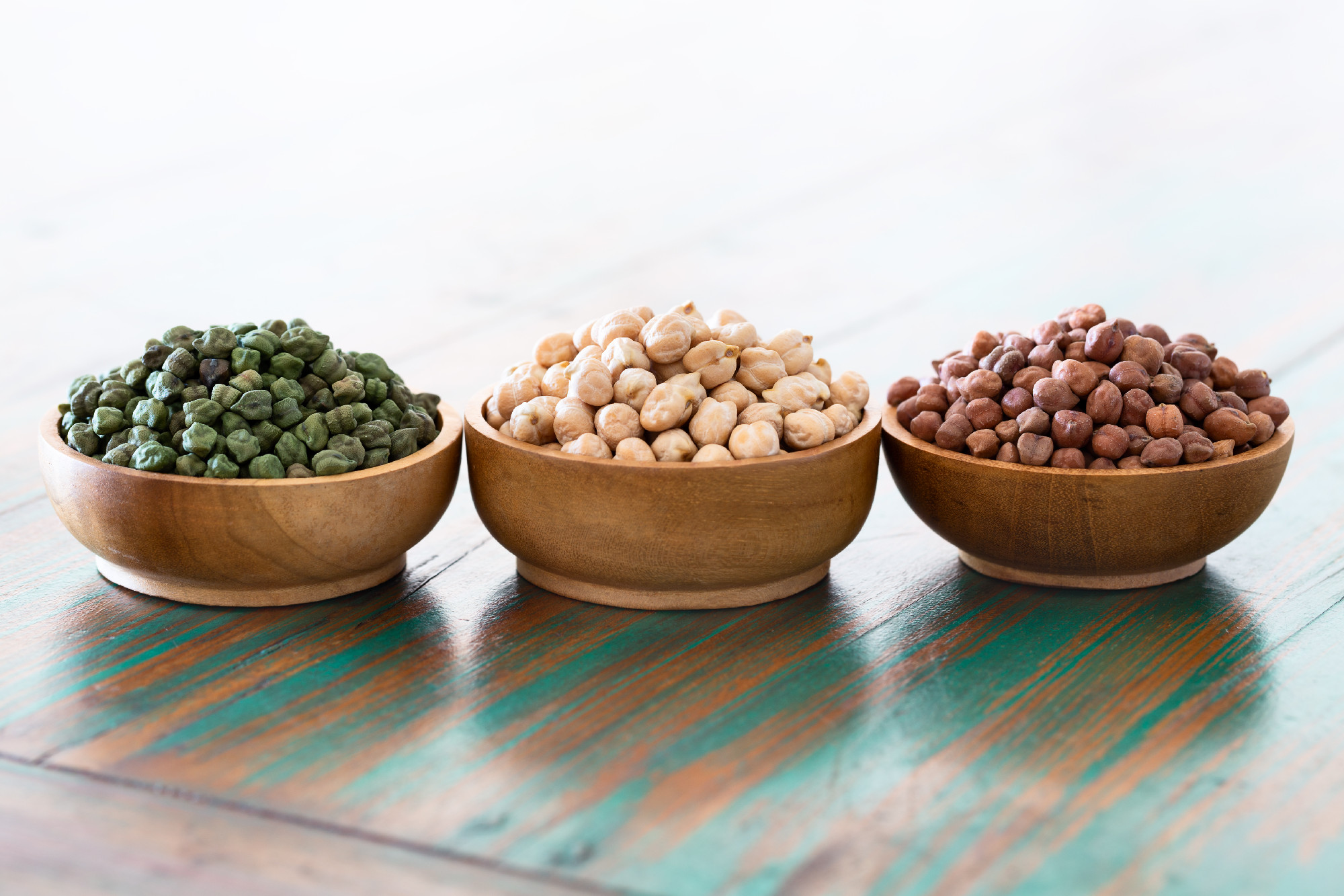 Colored chickpeas (red, green, white) in wooden bowls on rustic 